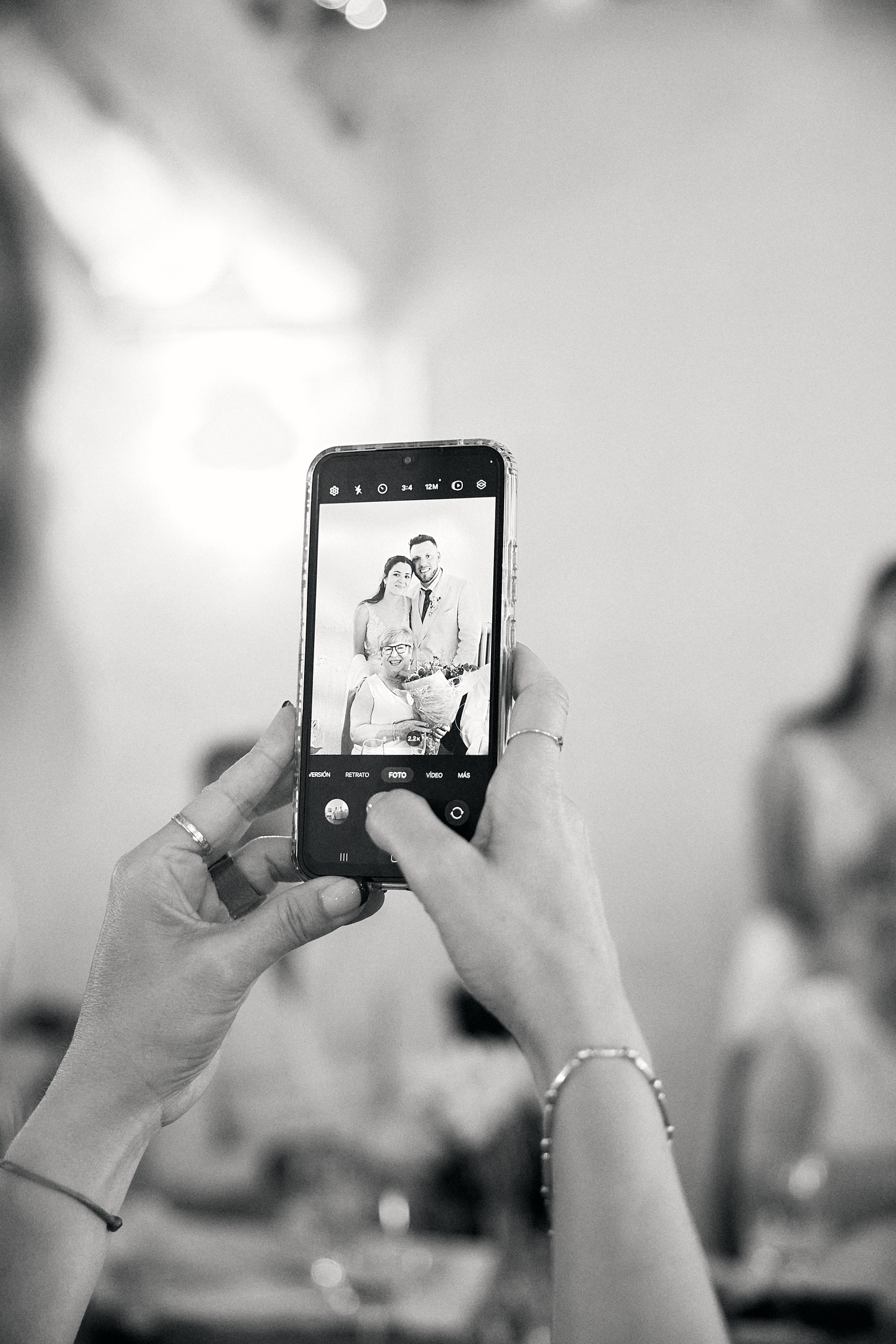 Black and white candid photograph of a wedding guest capturing the celebration on a phone.