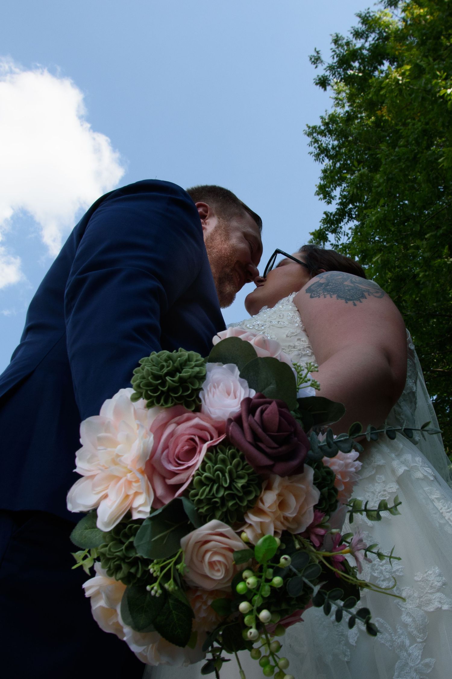 Groom kissing bride from below angle with colorful wedding bouquet of pink and purple roses.