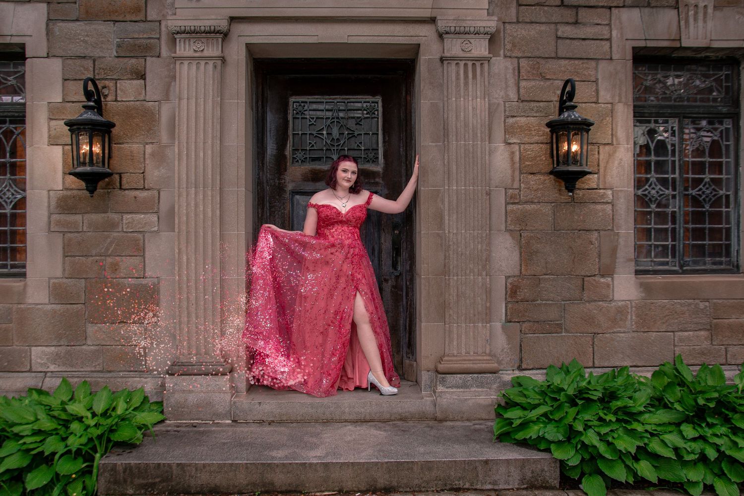 Woman in elegant red gown posing in stone archway with vintage lanterns at historic building.
