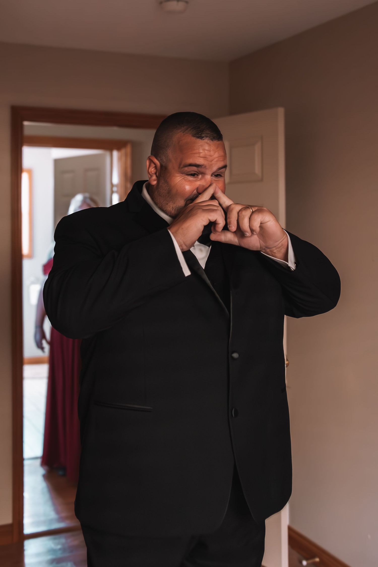 Emotional groom in black suit wiping tears during wedding preparations indoors.