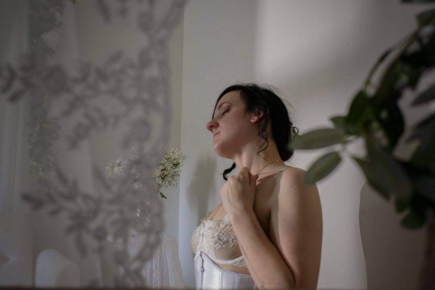 Woman in lace lingerie touching her neck in a serene white room.