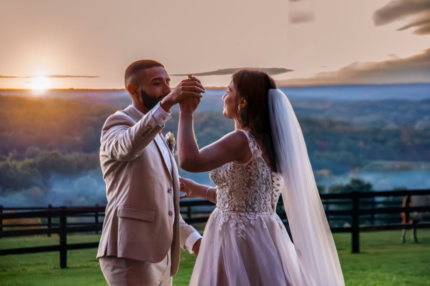 Bride and groom dancing at sunset with scenic countryside landscape in background.
