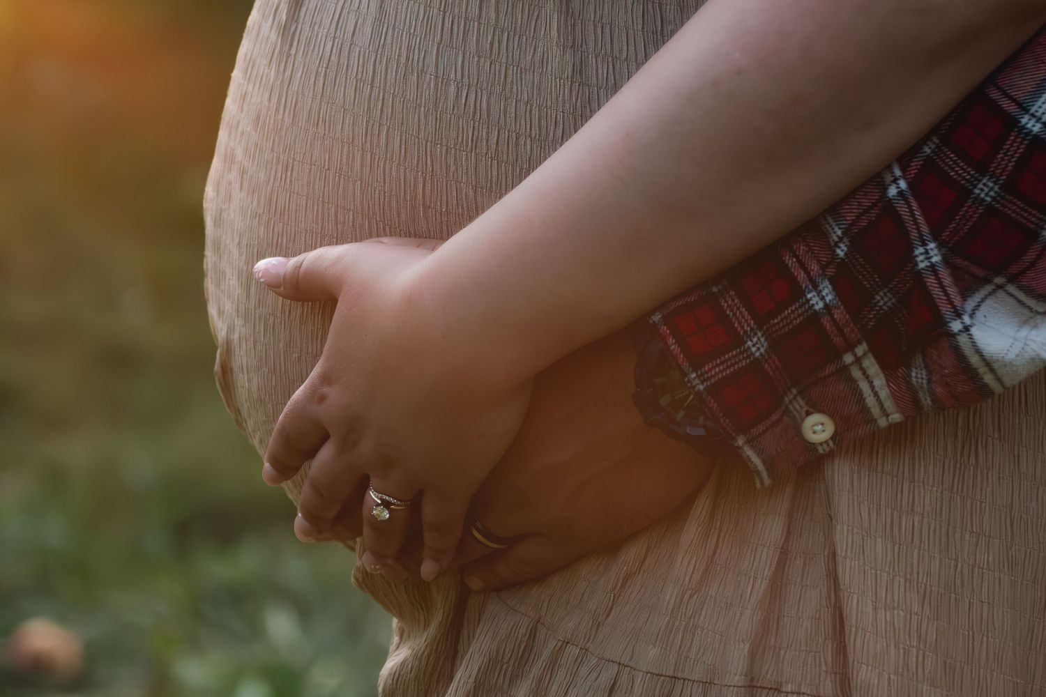 Close-up of pregnant woman cradling baby bump outdoors in warm golden sunset light.