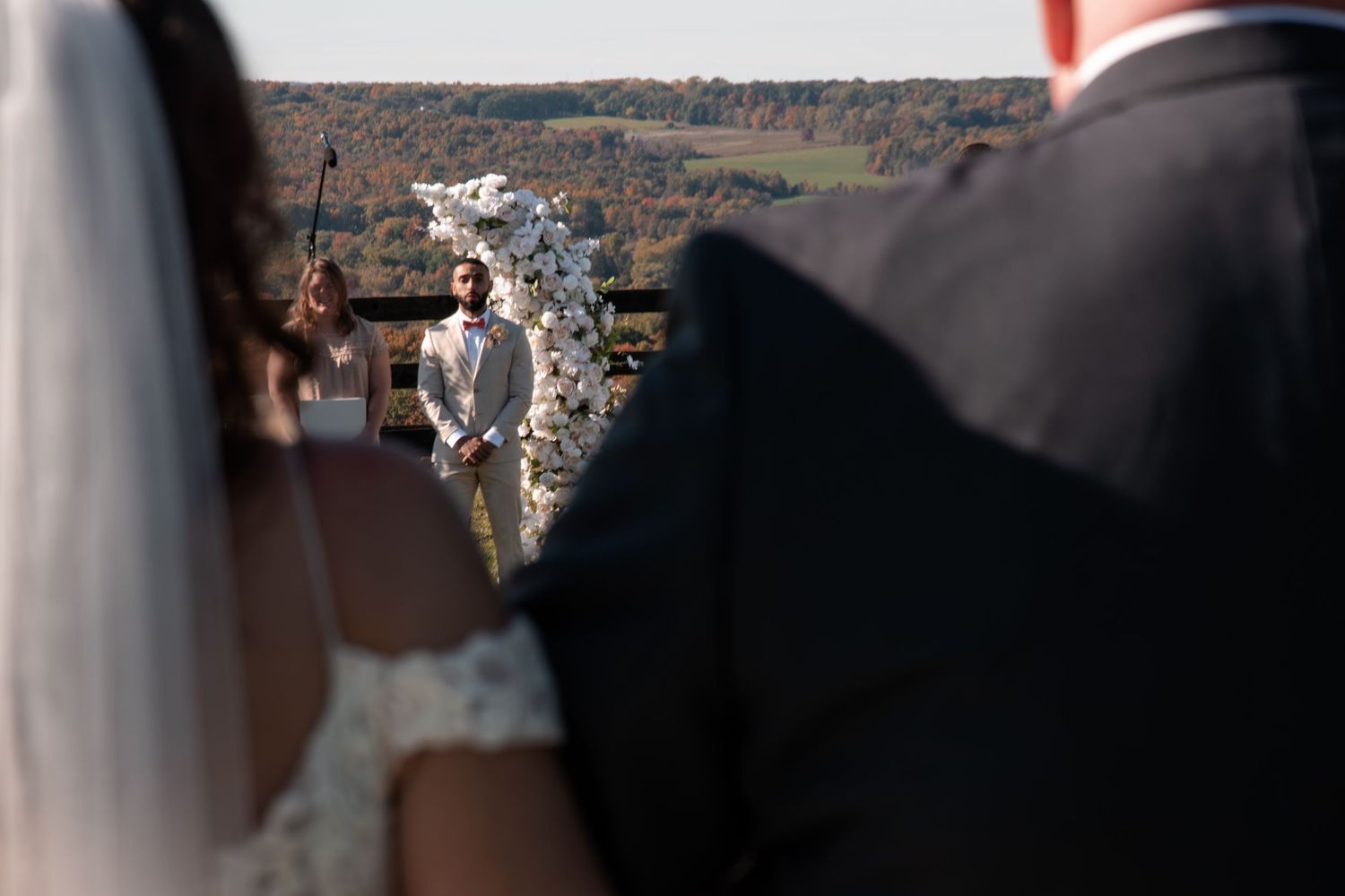 Bride and groom stand at outdoor altar with officiant and stunning fall foliage backdrop.