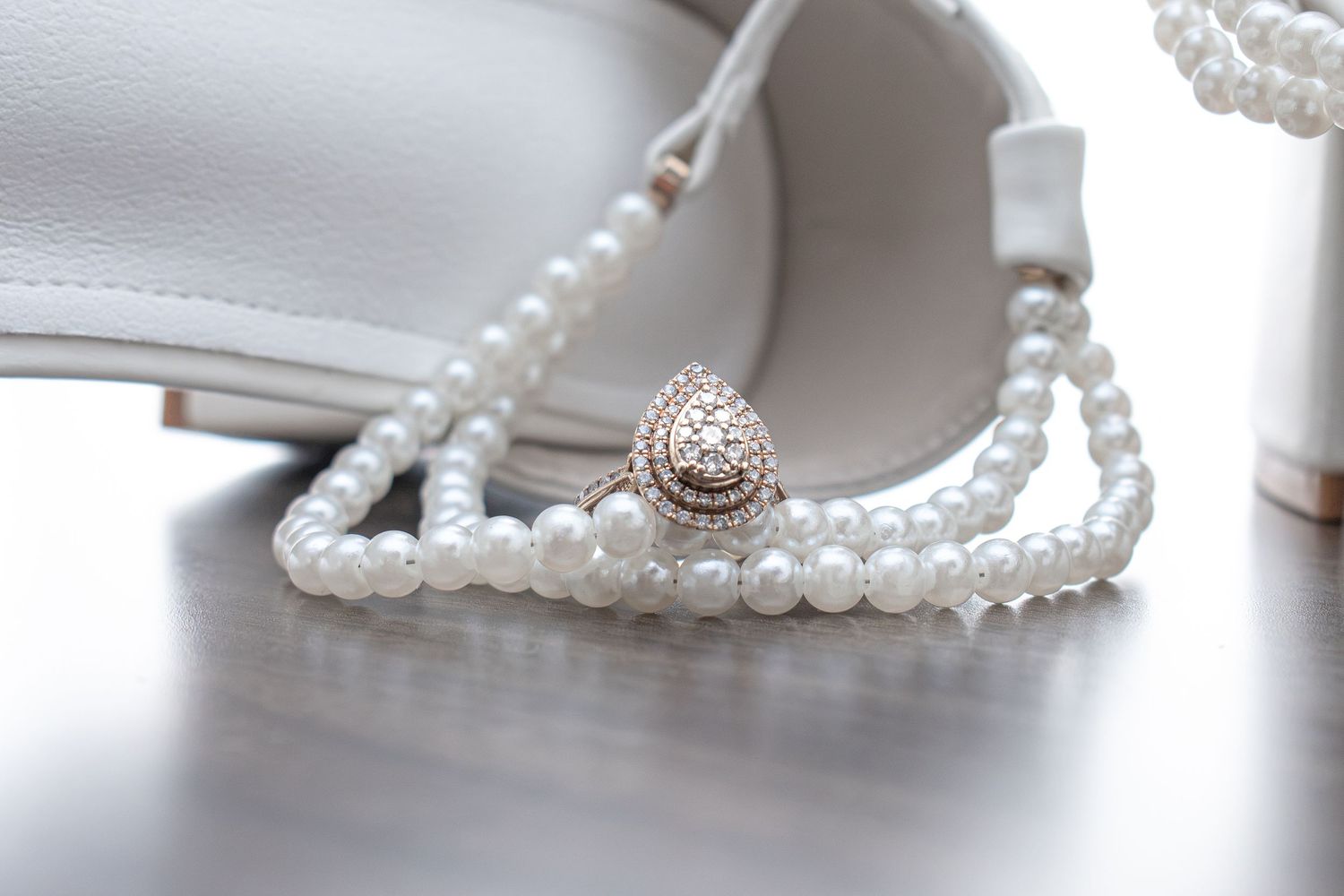Elegant white pearl necklace with decorative clasp displayed beside white bridal heels on a gray surface.