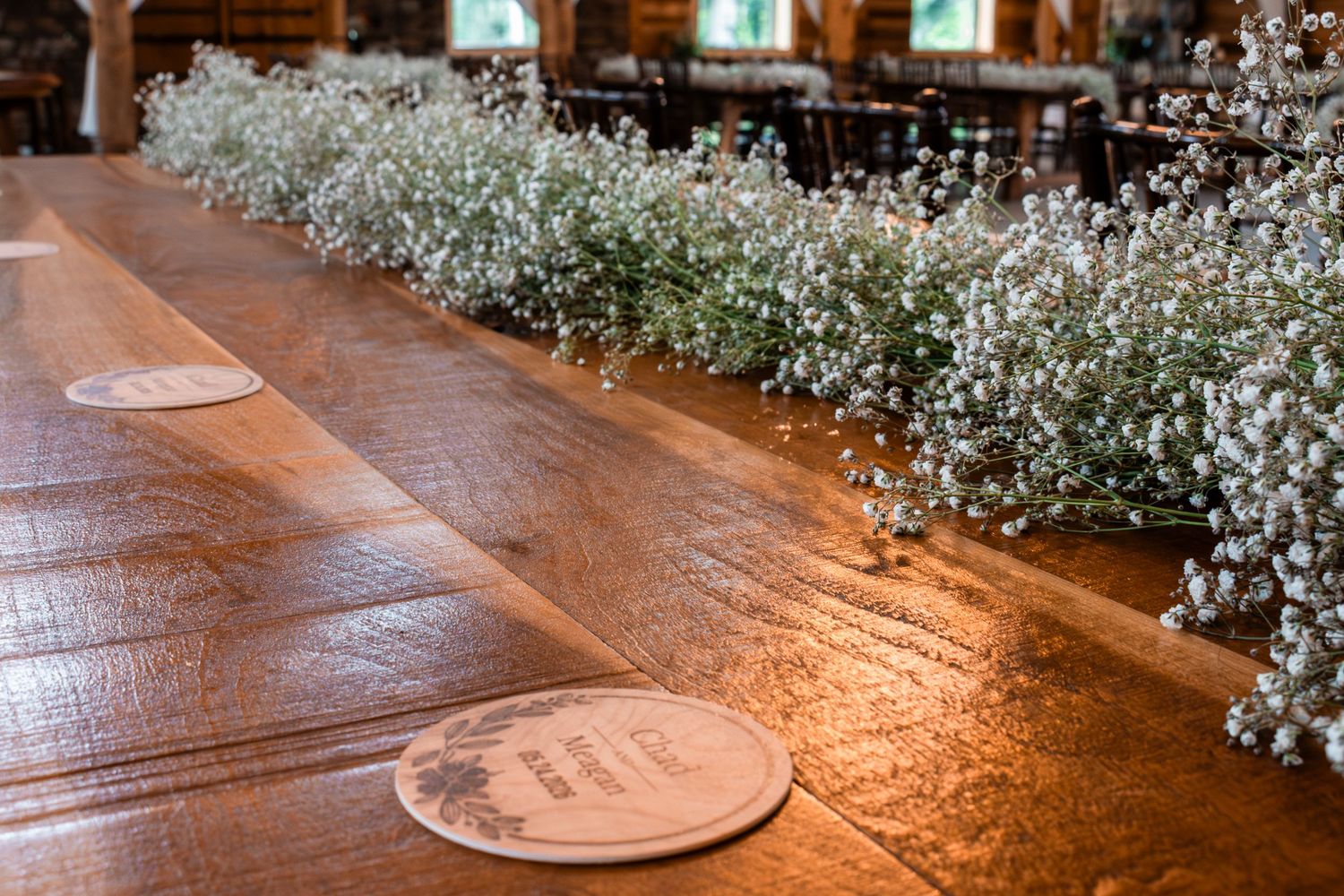 Rustic wooden table decorated with baby's breath flowers and personalized coasters at a wedding reception.