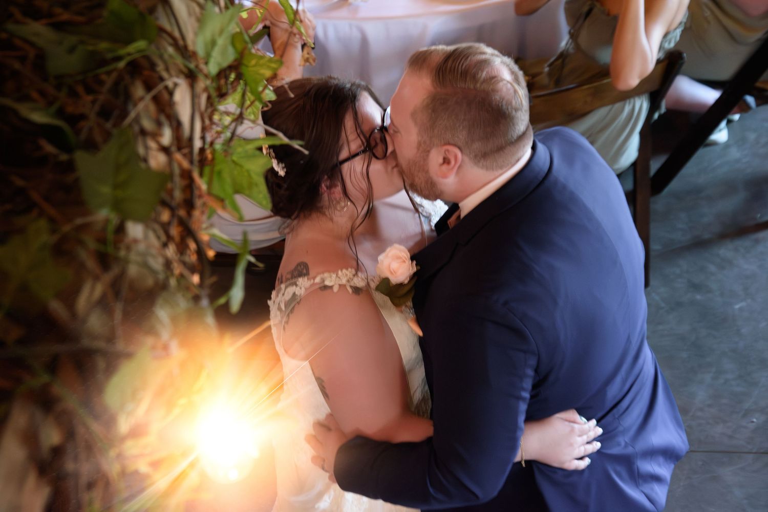 Bride and groom share their first kiss during wedding ceremony surrounded by warm glowing lights.