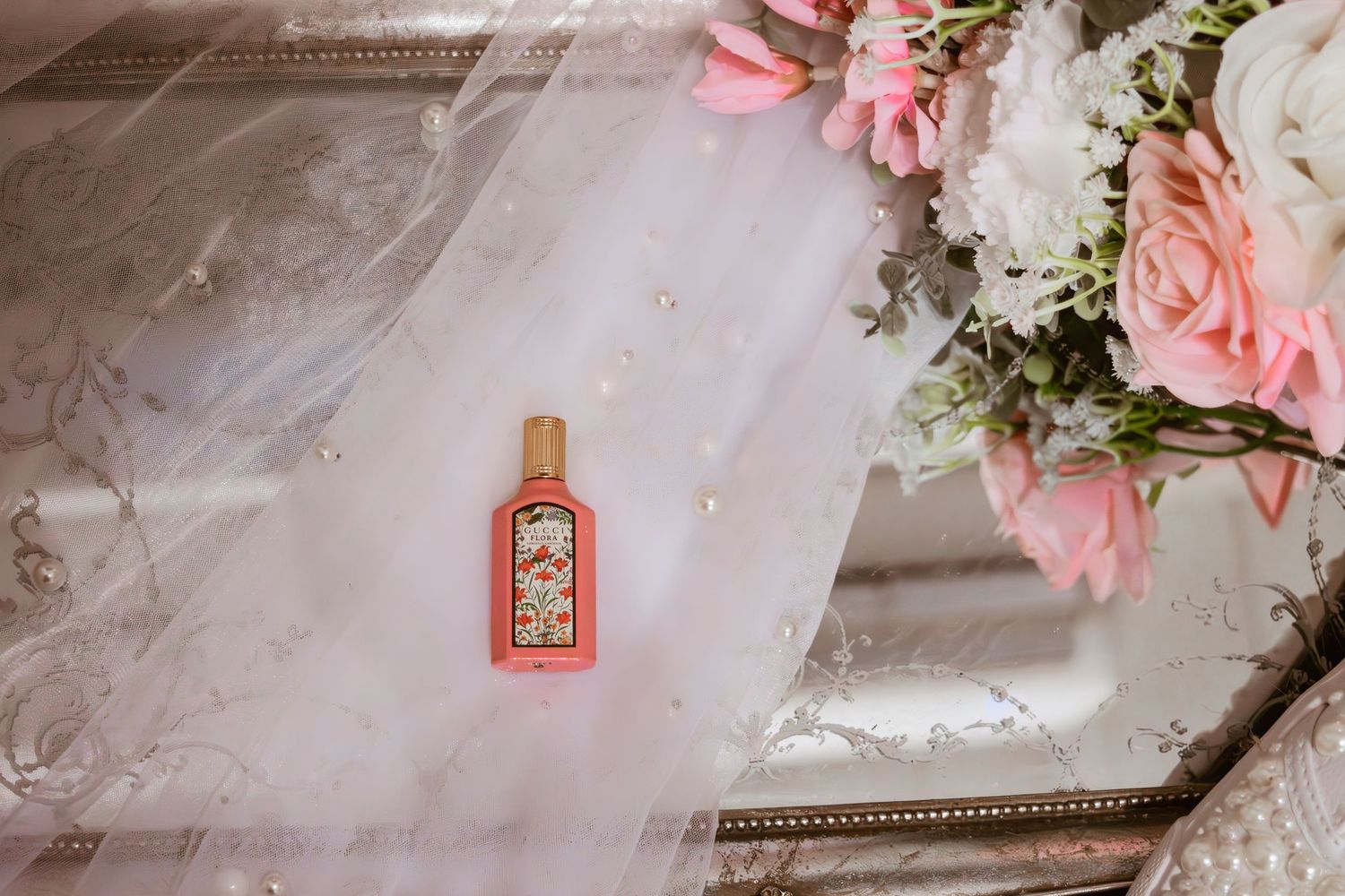 Pink Gucci perfume bottle on a silver tray with a white veil and pink roses bouquet.