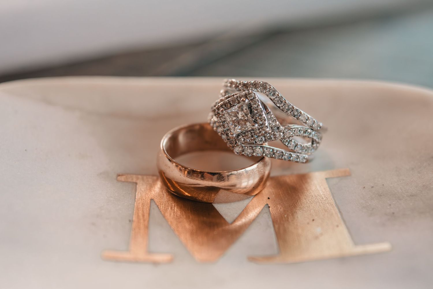 Close-up of diamond wedding ring and gold band resting on a personalized ceramic dish engraved with the letter M.