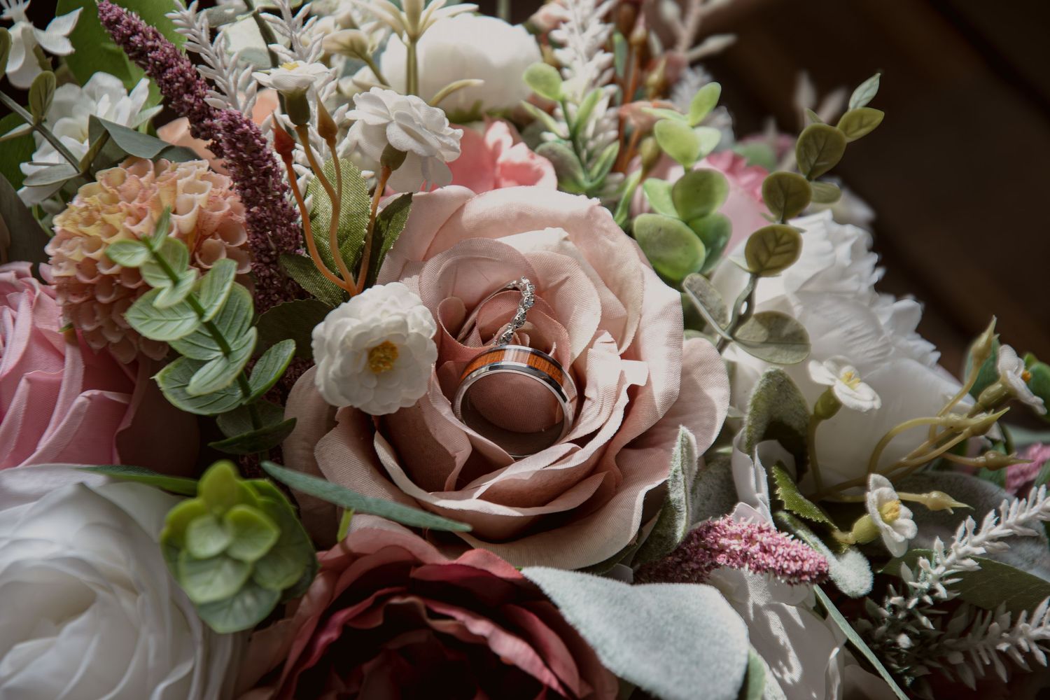 Gold wedding bands resting inside a blush pink rose in a romantic bridal bouquet arrangement.