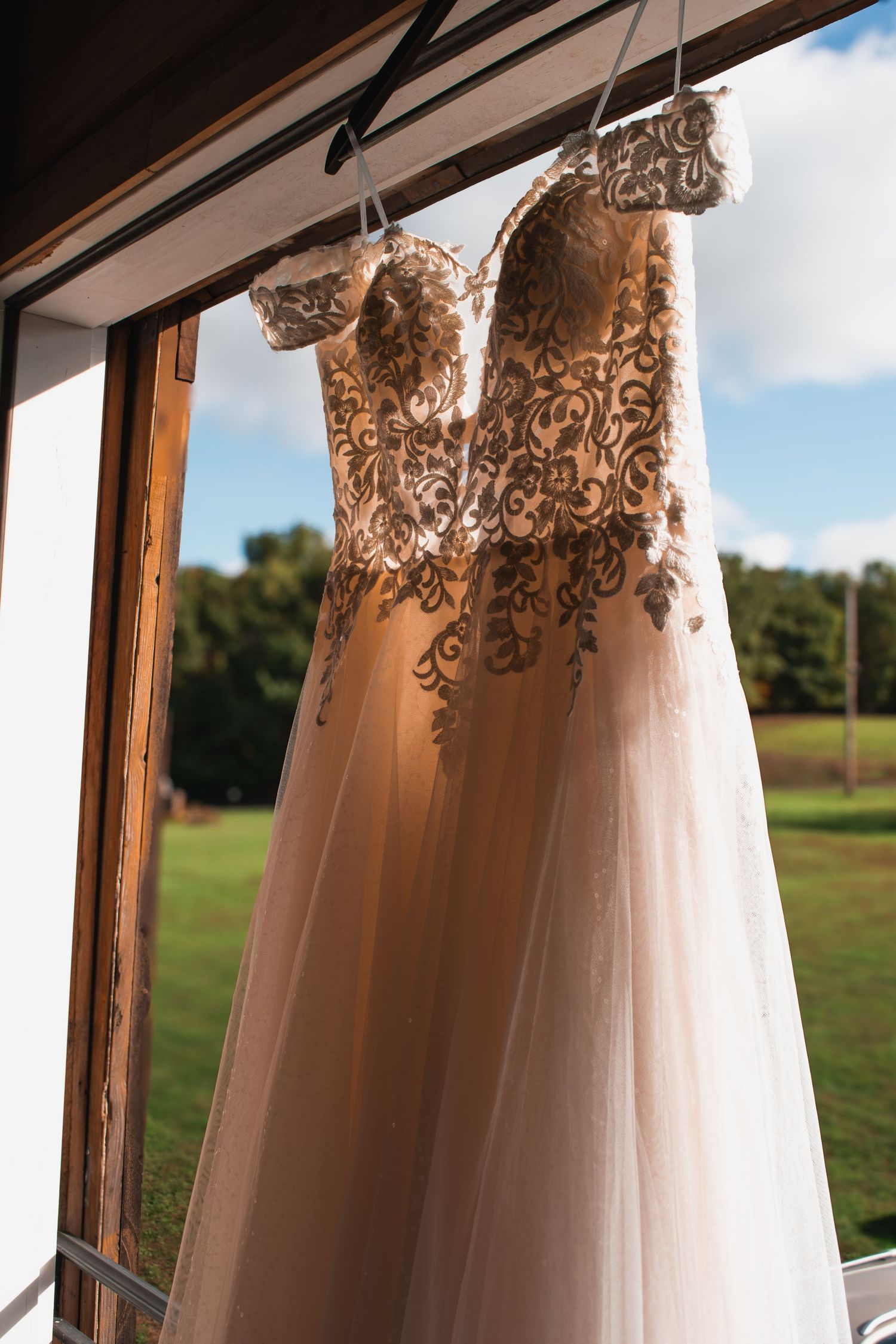 Elegant lace wedding dress hanging by a window with a scenic green landscape backdrop.