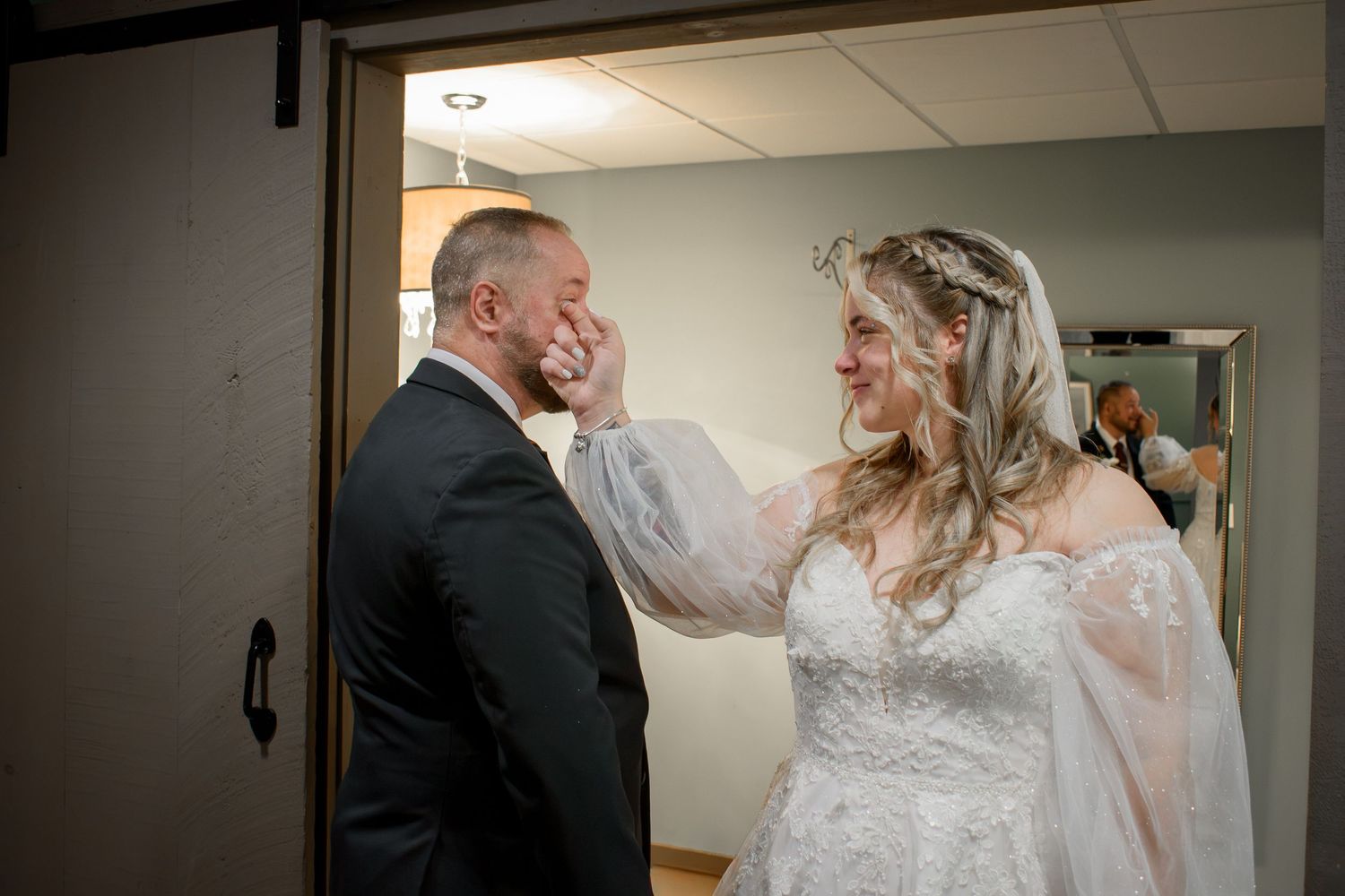 Bride in lace wedding gown tenderly touches grooms face during emotional first look moment before ceremony.