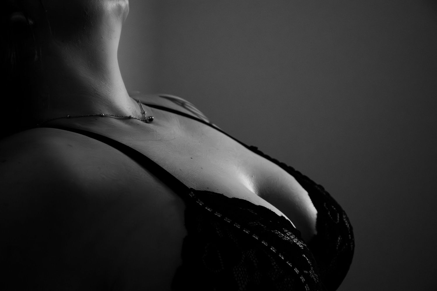 Black and white close-up of a woman in a lace bra showcasing a delicate necklace and décolletage.