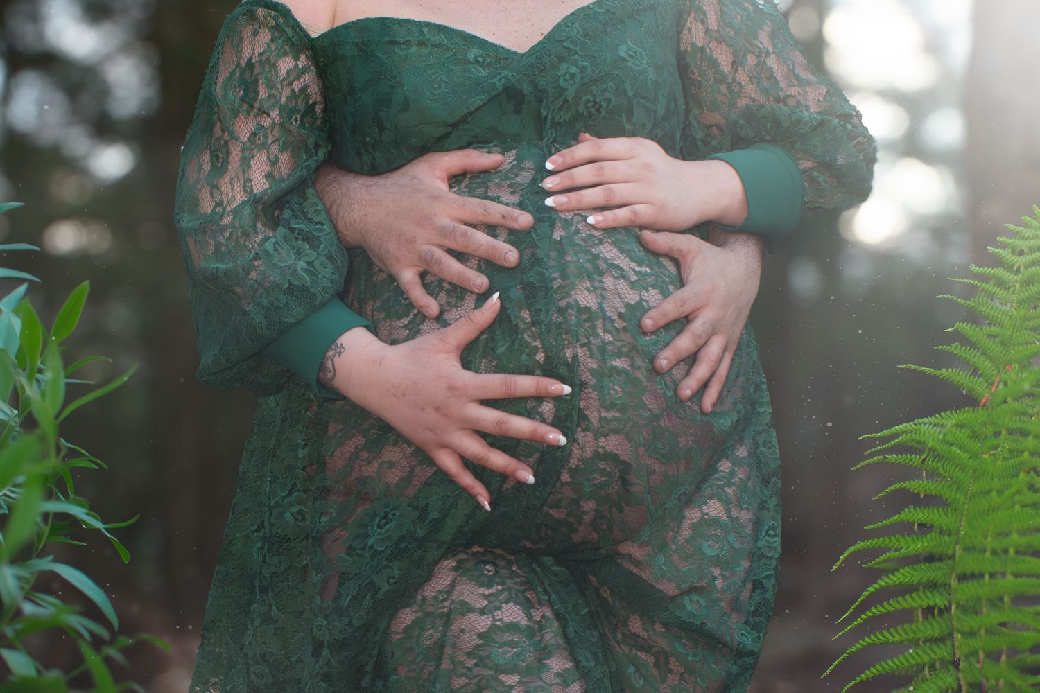 Pregnant woman in green lace dress cradling baby bump outdoors.