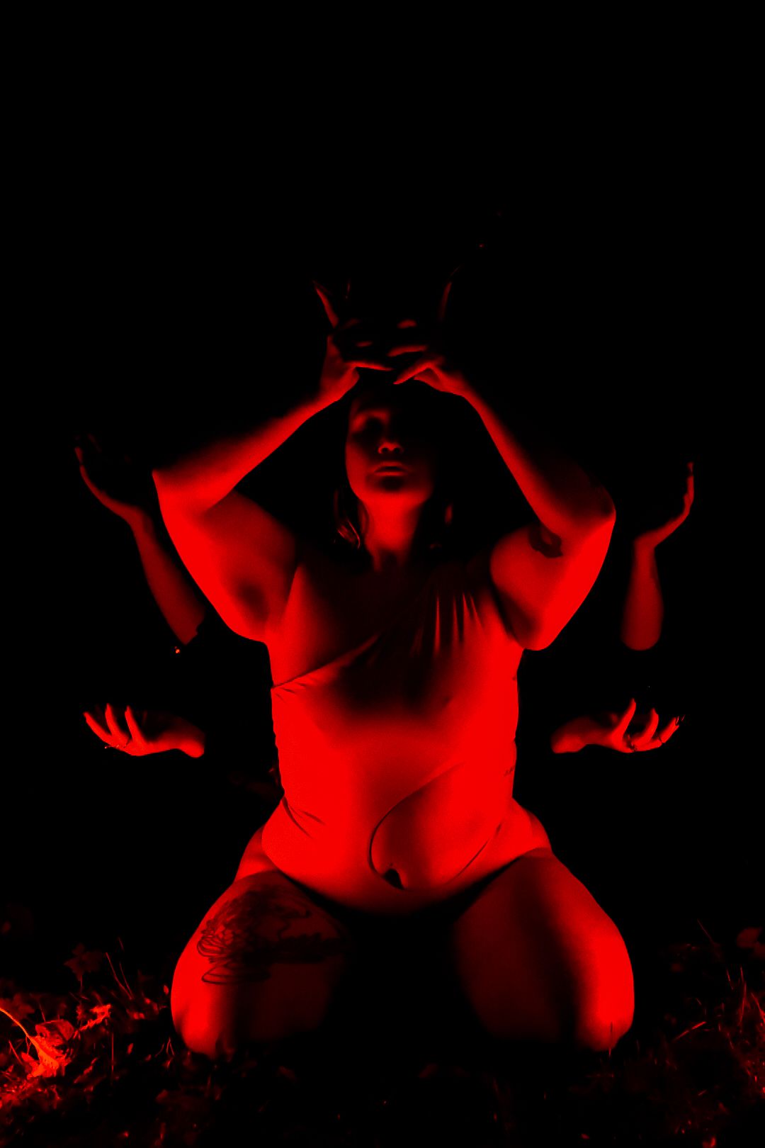 Person illuminated in dramatic red light kneeling with hands raised in an artistic dark photography pose.