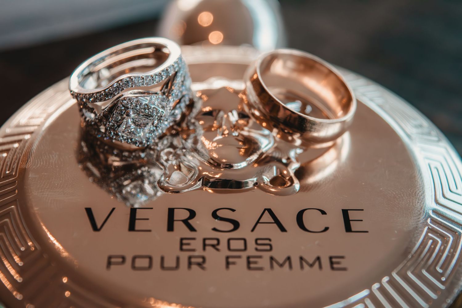 Versace Eros Pour Femme perfume lid displaying elegant gold and silver engagement rings and wedding bands.