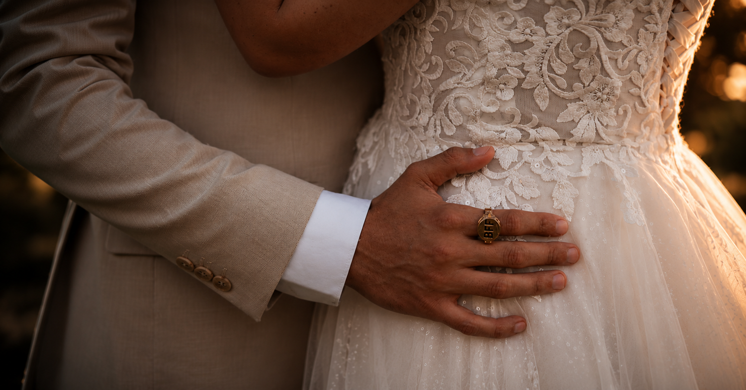 Close-up of a bride and groom embracing, showcasing lace wedding dress and groom's ring.