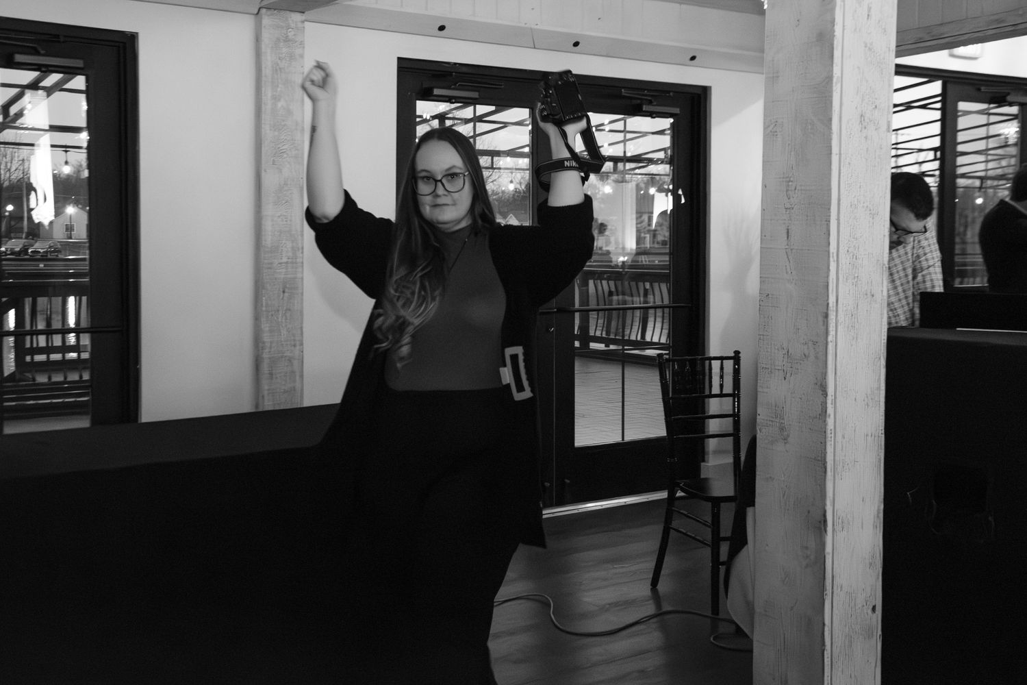 Woman celebrating with raised fist in black and white photo at wedding reception.