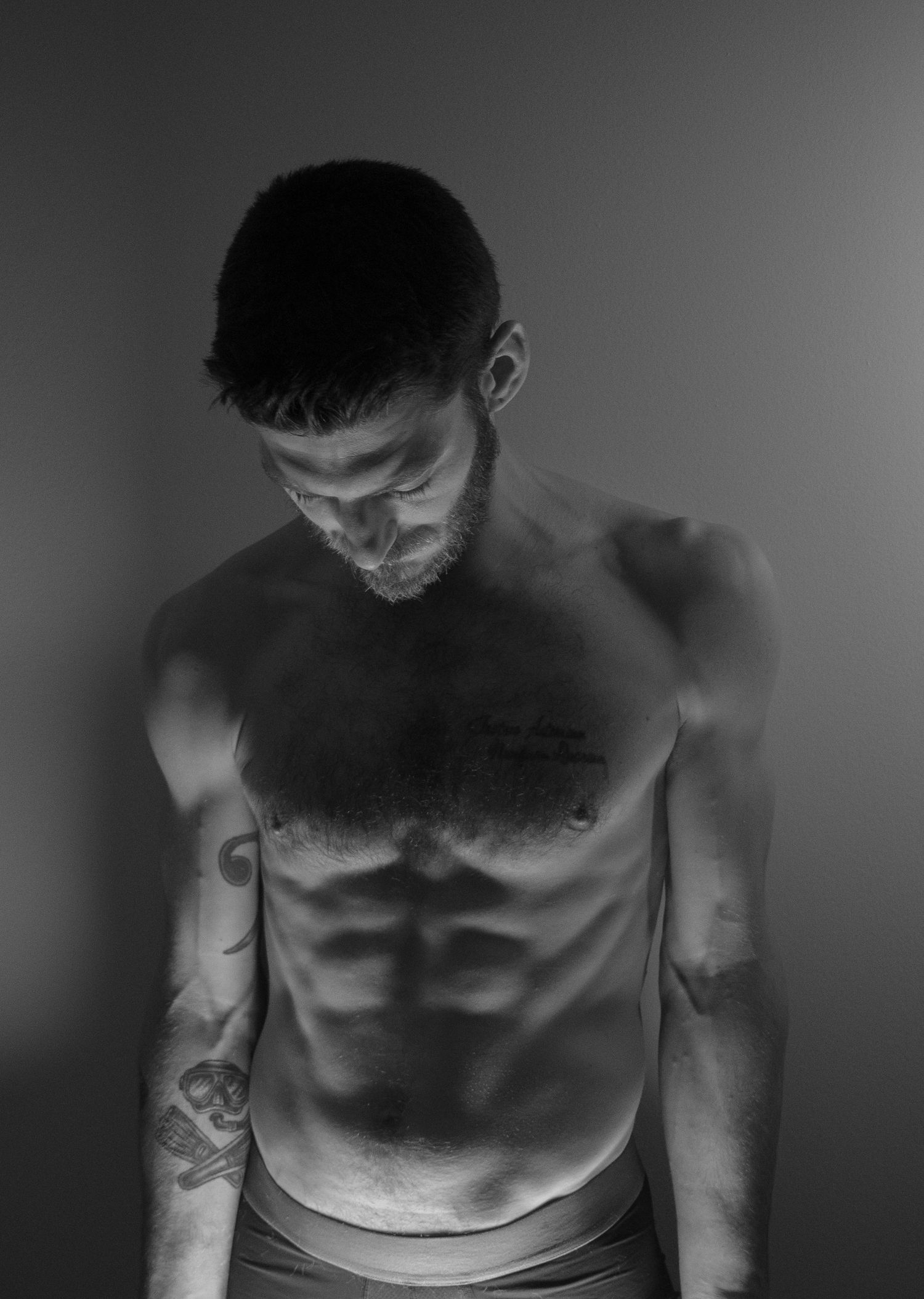 Black and white photo of a tattooed shirtless man with defined abs looking down.