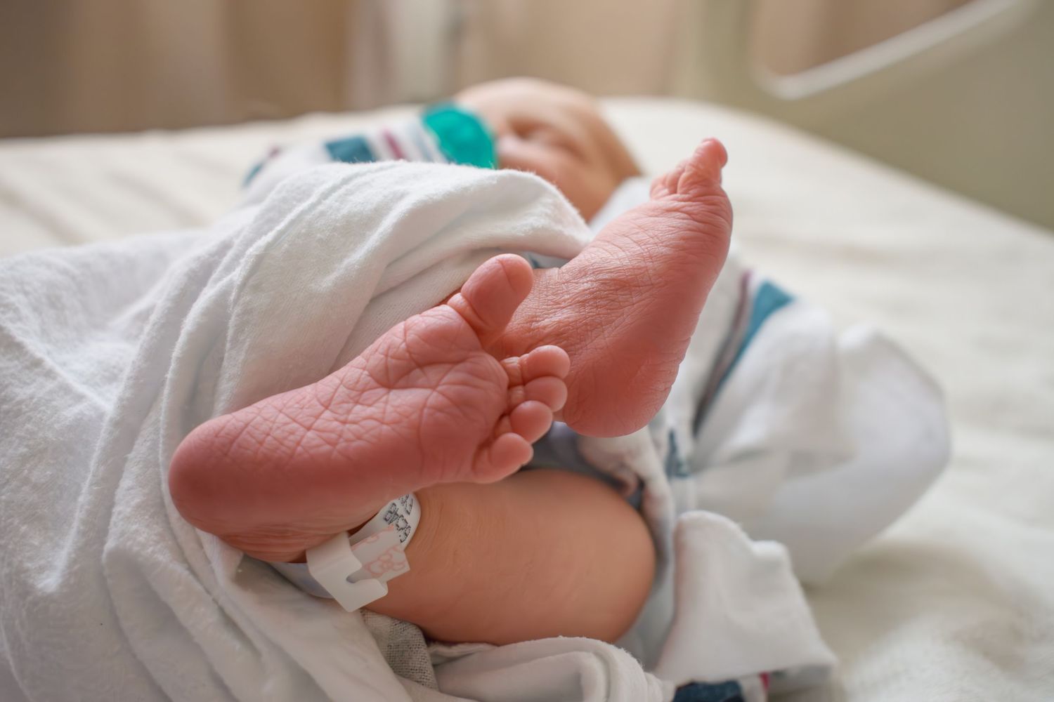 Close-up of newborn baby feet wrapped in a white blanket in a hospital bed.