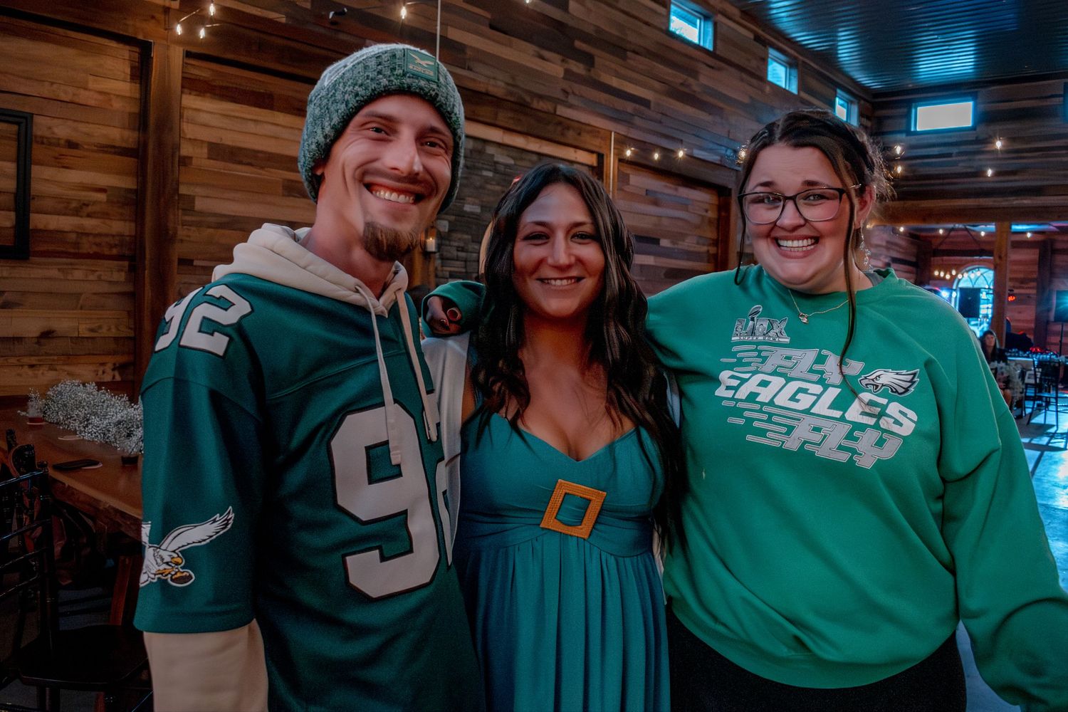Three friends posing together wearing Philadelphia Eagles green jerseys and shirts at a sports bar gathering.