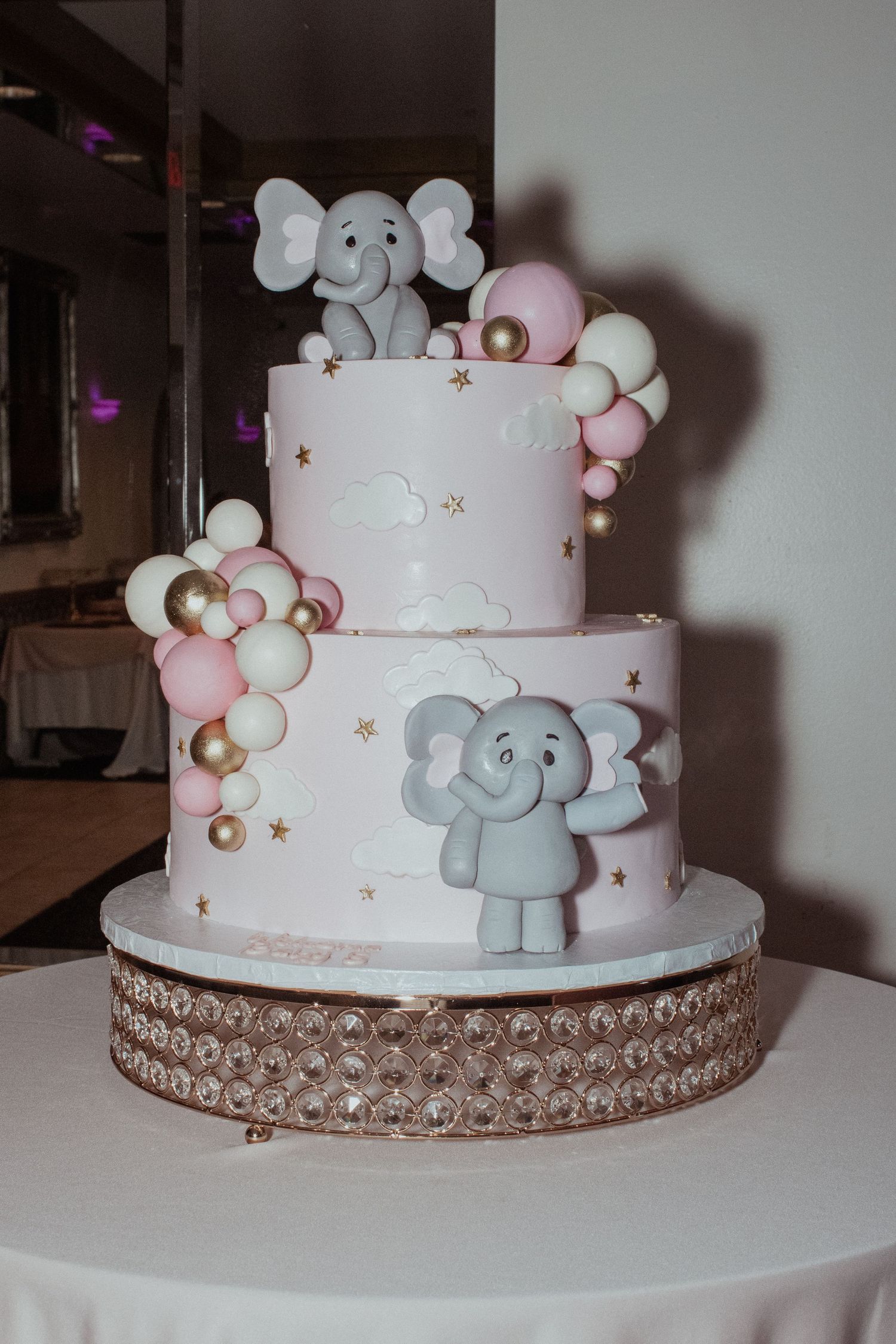 Two-tiered white baby shower cake with gray elephant decorations and pearl border.