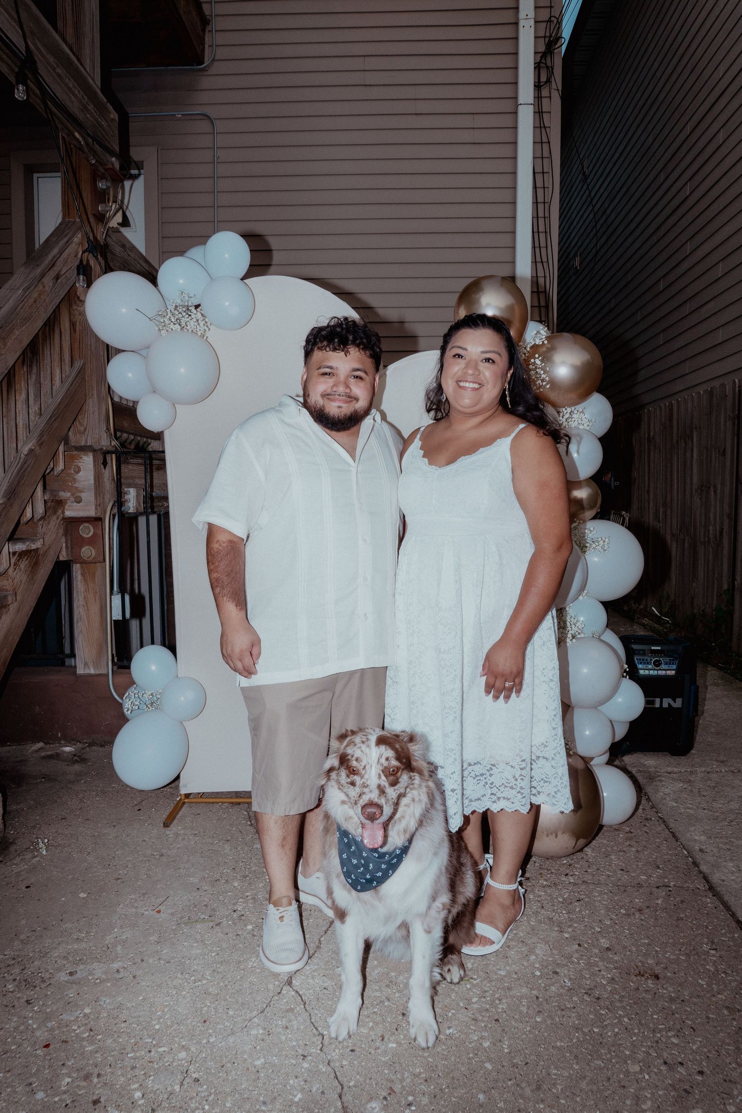 Party guests in white outfits posing with balloon decorations at a nighttime event.