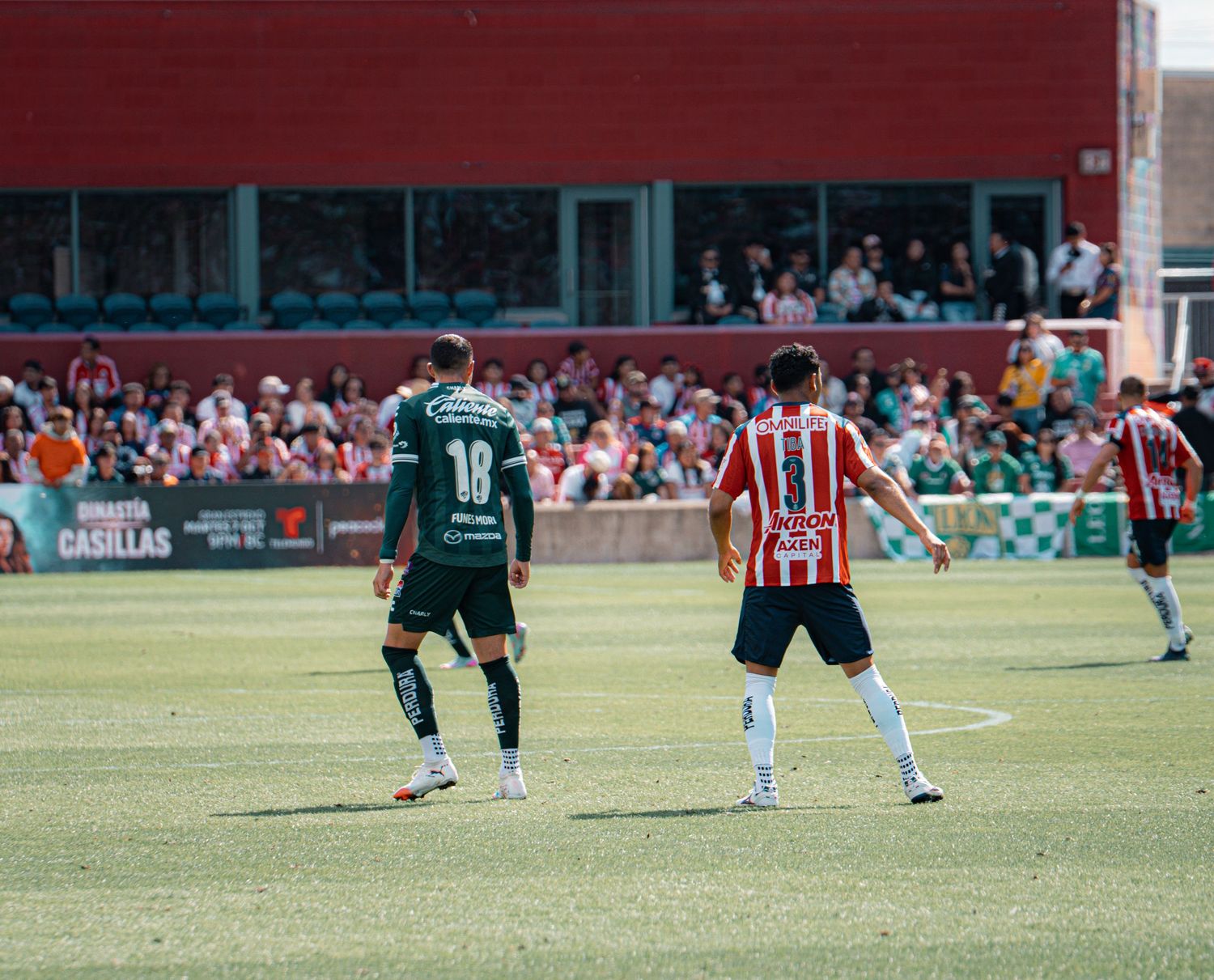 Soccer players from opposing teams compete on a sunny field during a match.