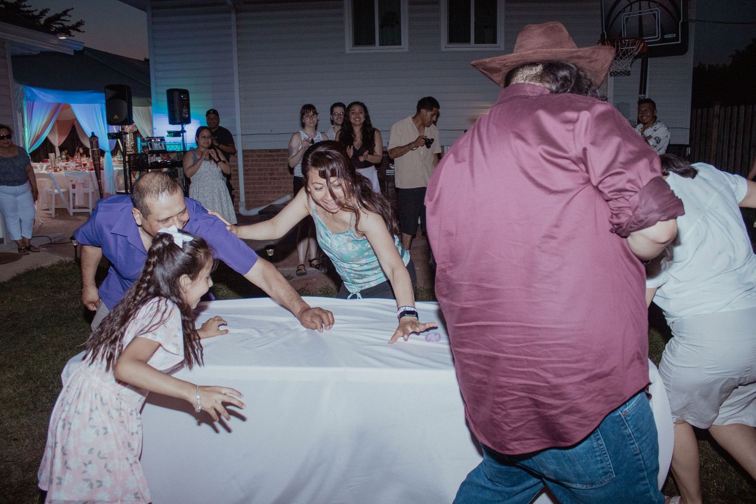 Outdoor evening party scene with white tablecloth setup.
