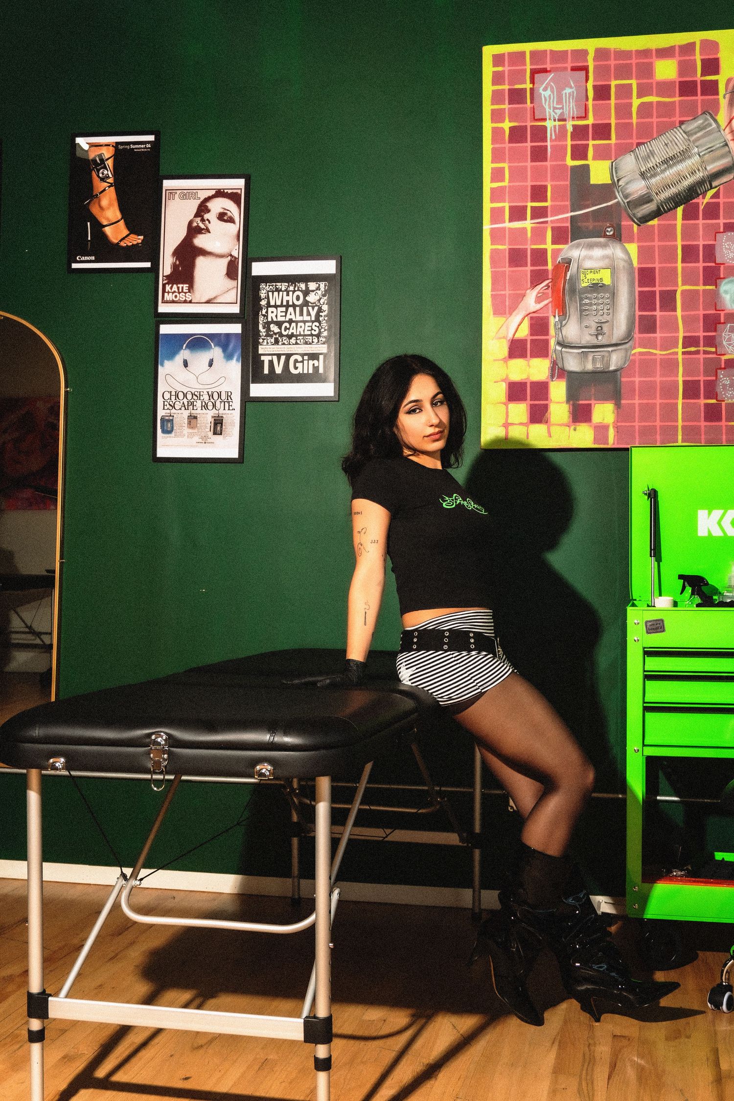 Studio setup with green walls, pink tile accent, and black furniture in moody lighting.