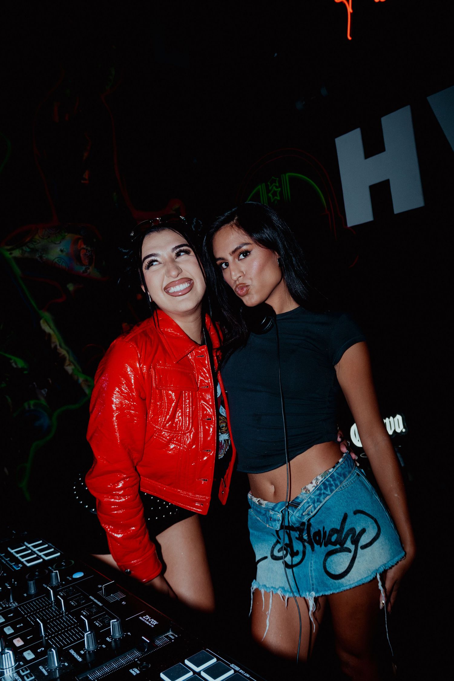 Club performers working DJ equipment in contrasting red and black outfits.