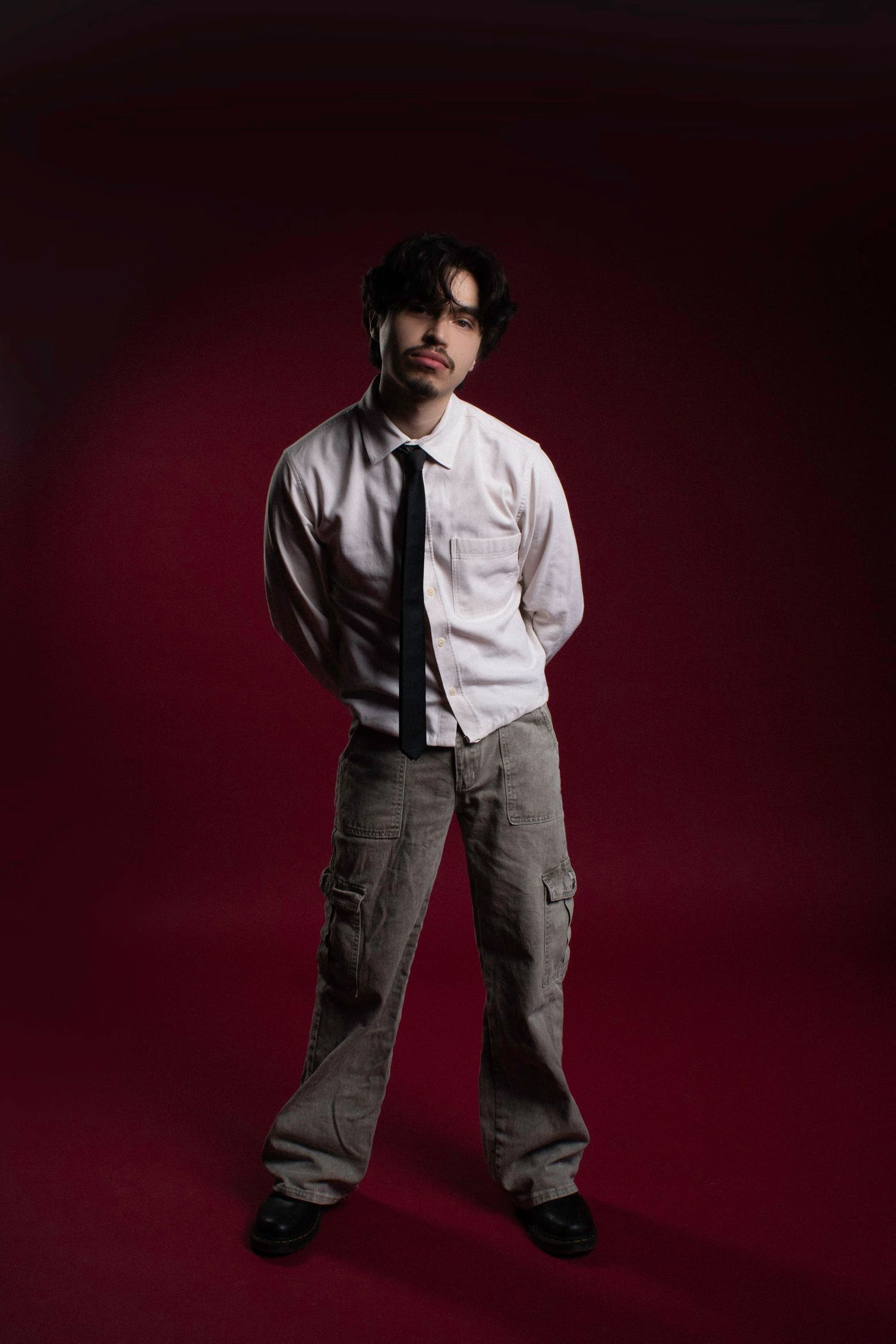 Person in white shirt and cargo pants posing dramatically against dark red background.