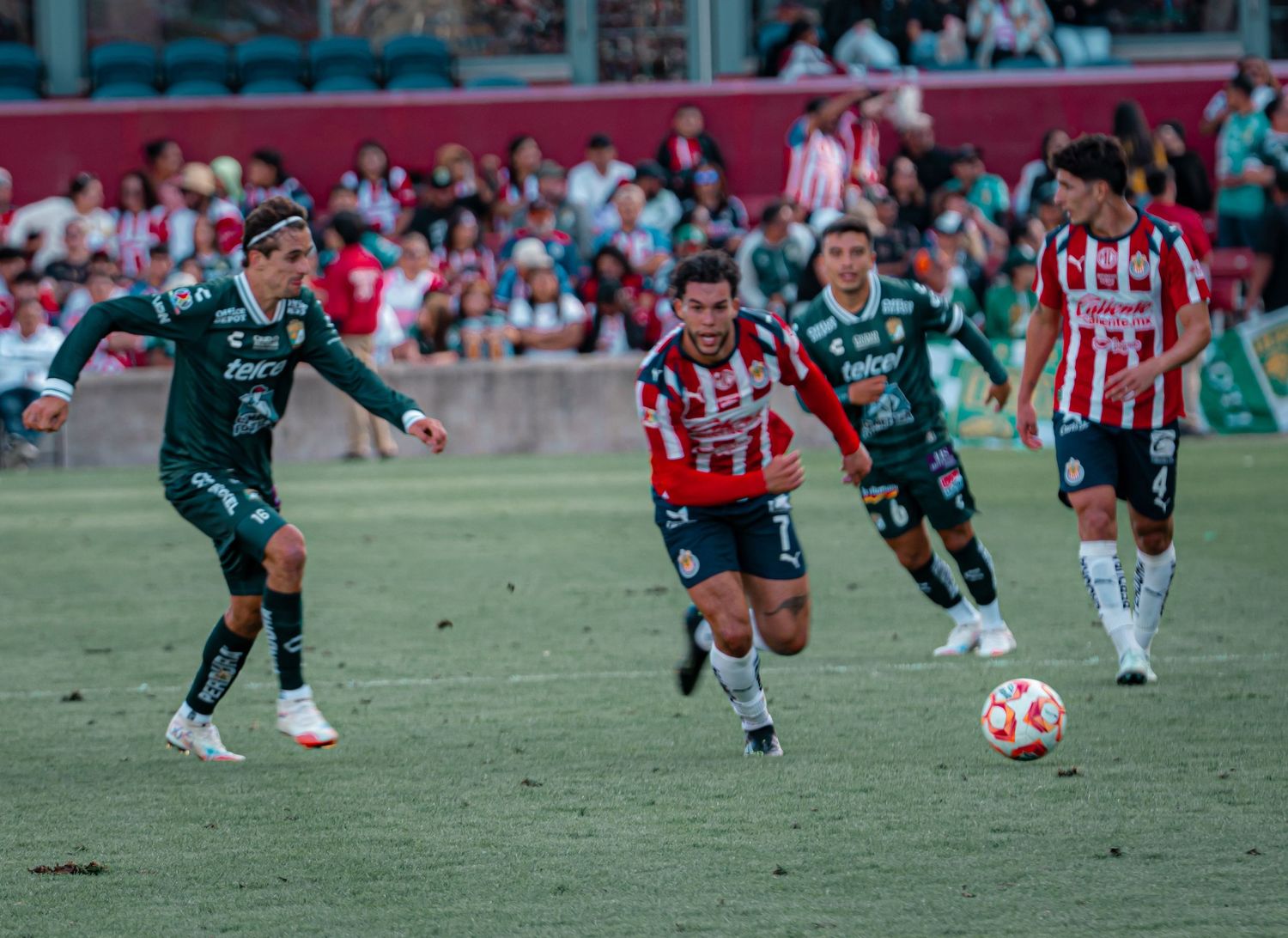 Soccer players from opposing teams battle for possession of the ball during intense match.