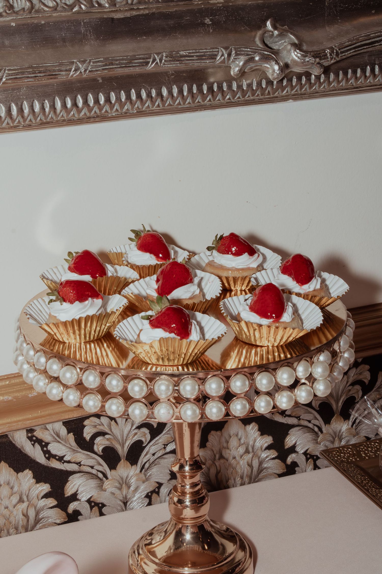 Gold cake stands decorated with pearls and topped with strawberry desserts.