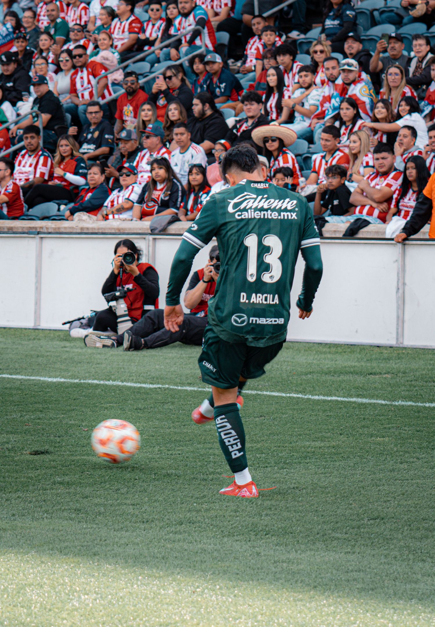 Soccer player takes a shot on goal during match with crowd watching in background.