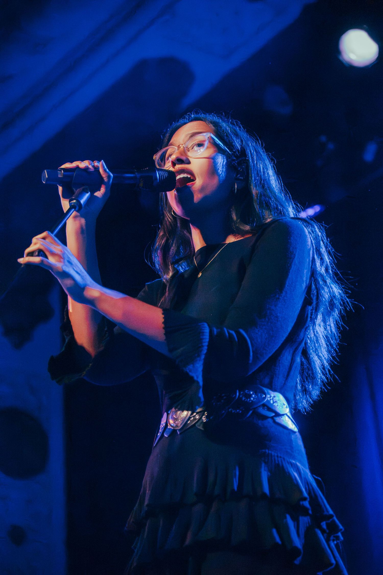 Concert performer singing passionately on stage illuminated by dramatic blue lighting.