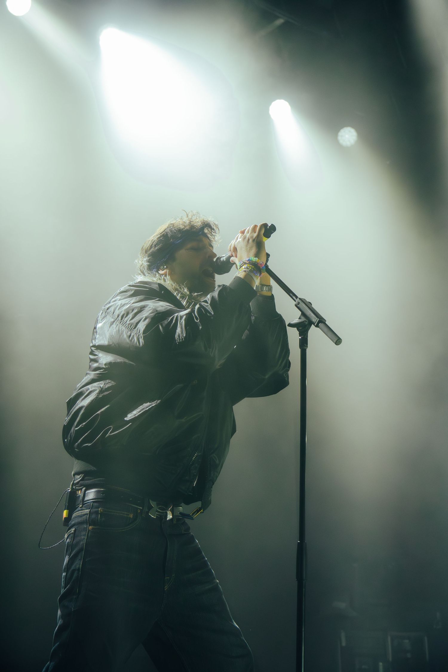 Silhouetted performer singing passionately on stage with dramatic backlighting and fog effects in a concert setting.