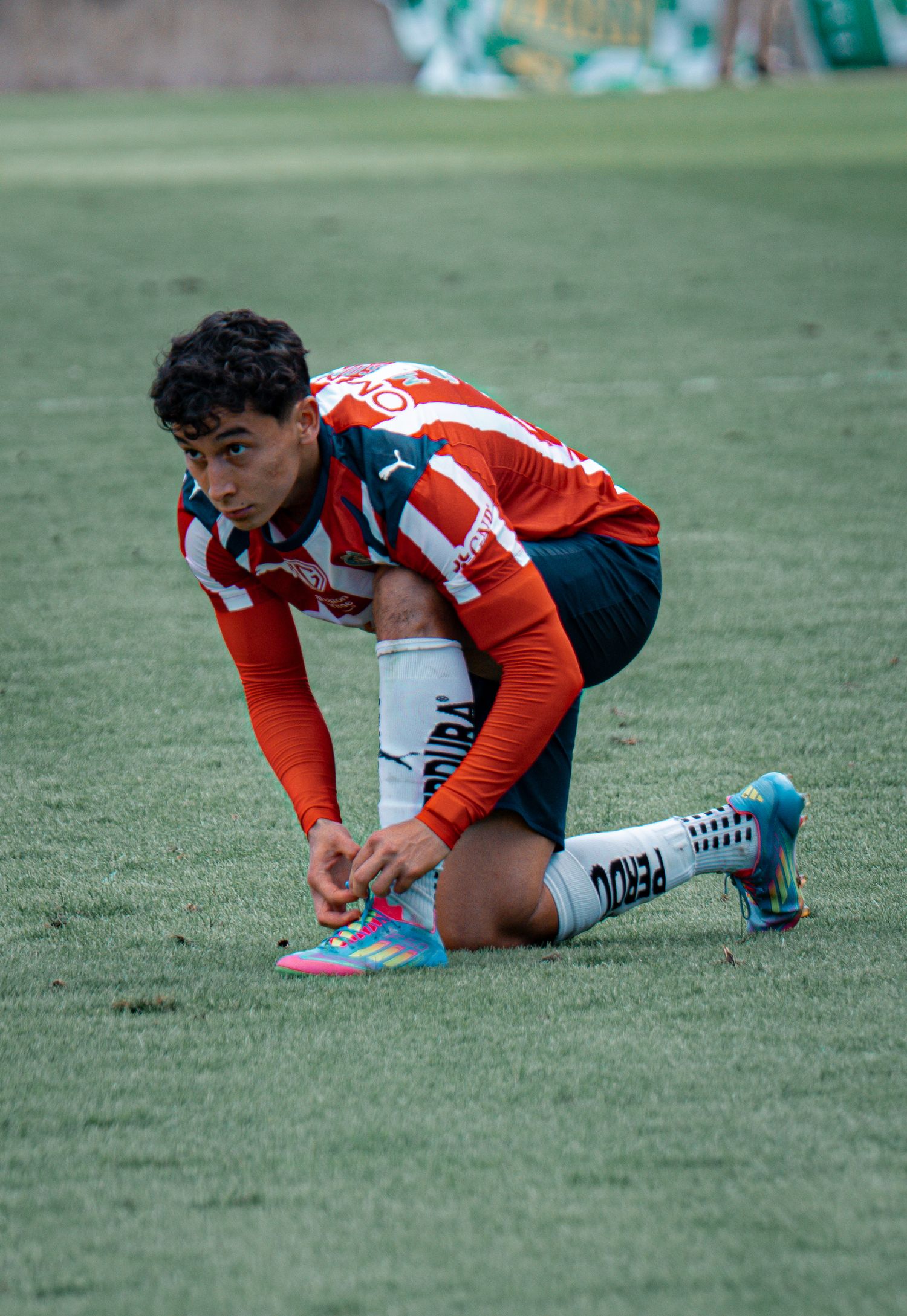 Player in red and white striped jersey kneels on soccer field during game.