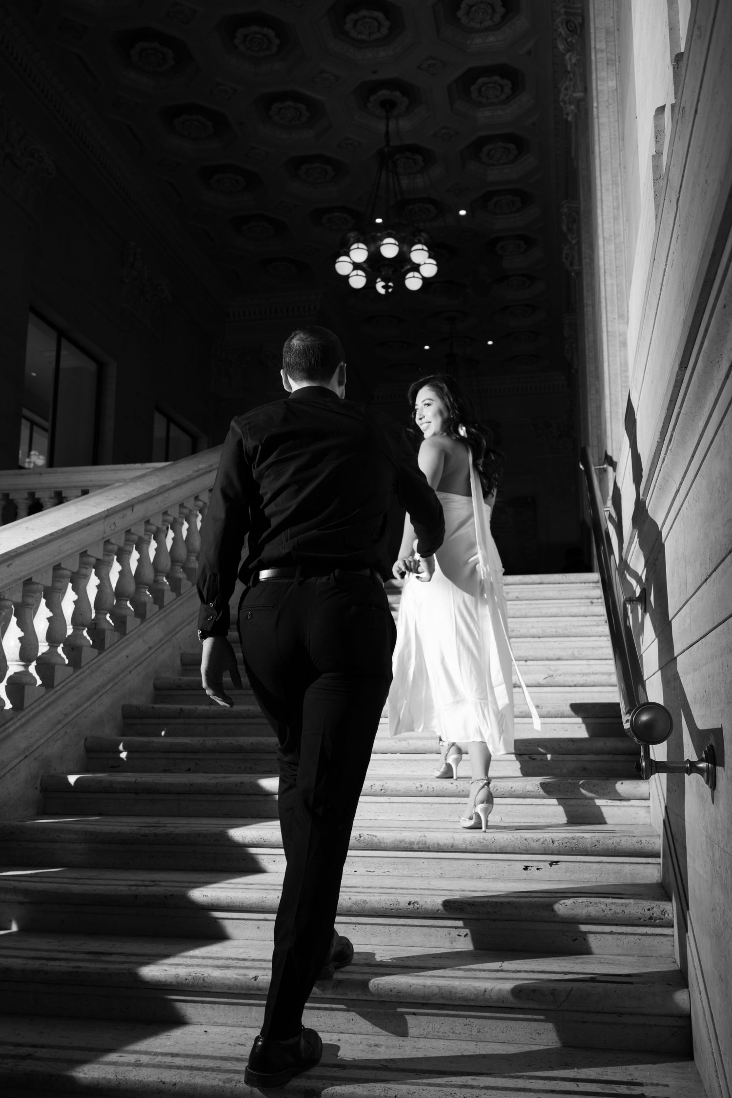 Black and white photo of figures ascending a grand staircase with dramatic lighting and shadows.