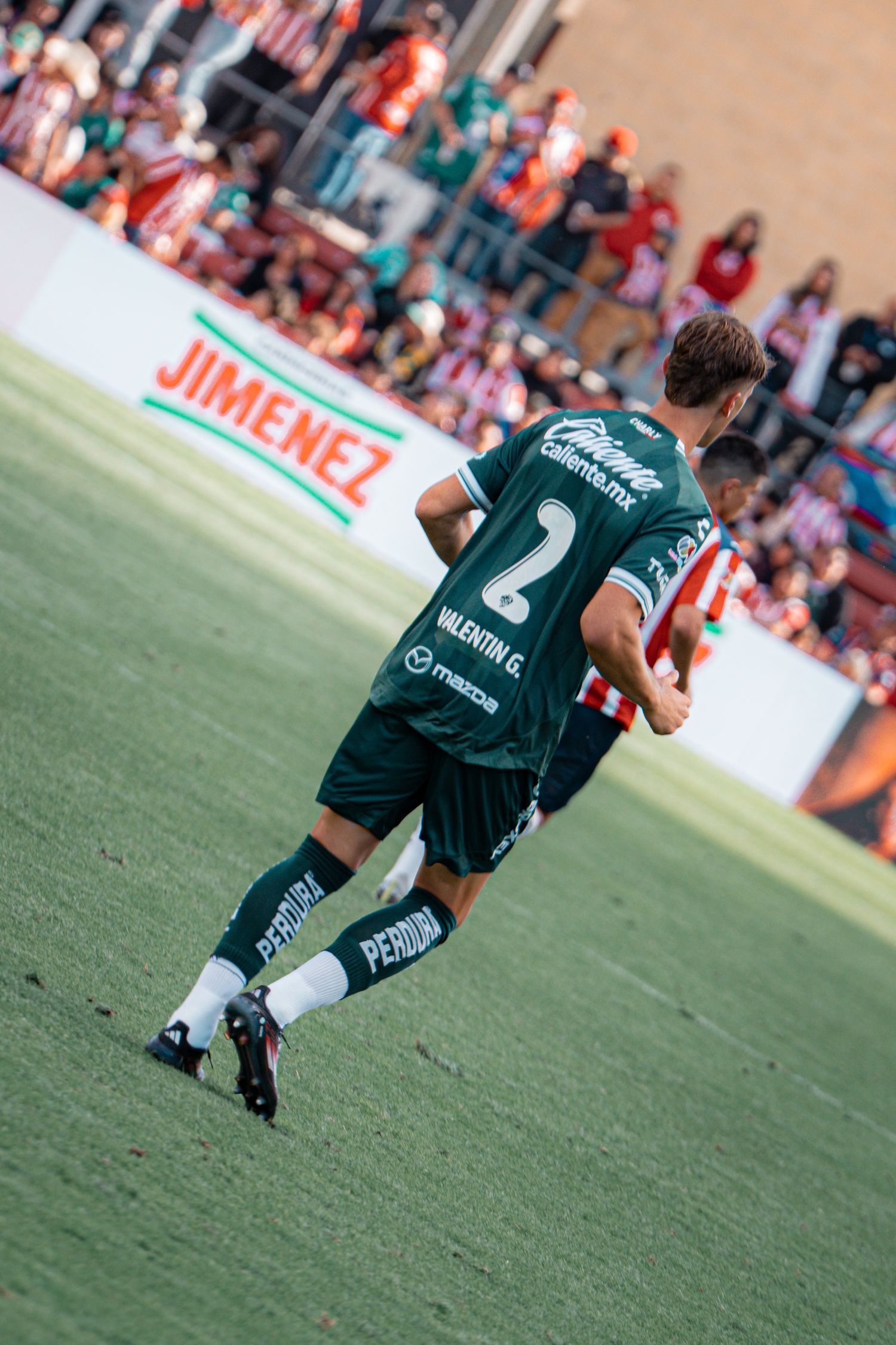 Soccer player in dark green uniform runs across grass field during match.