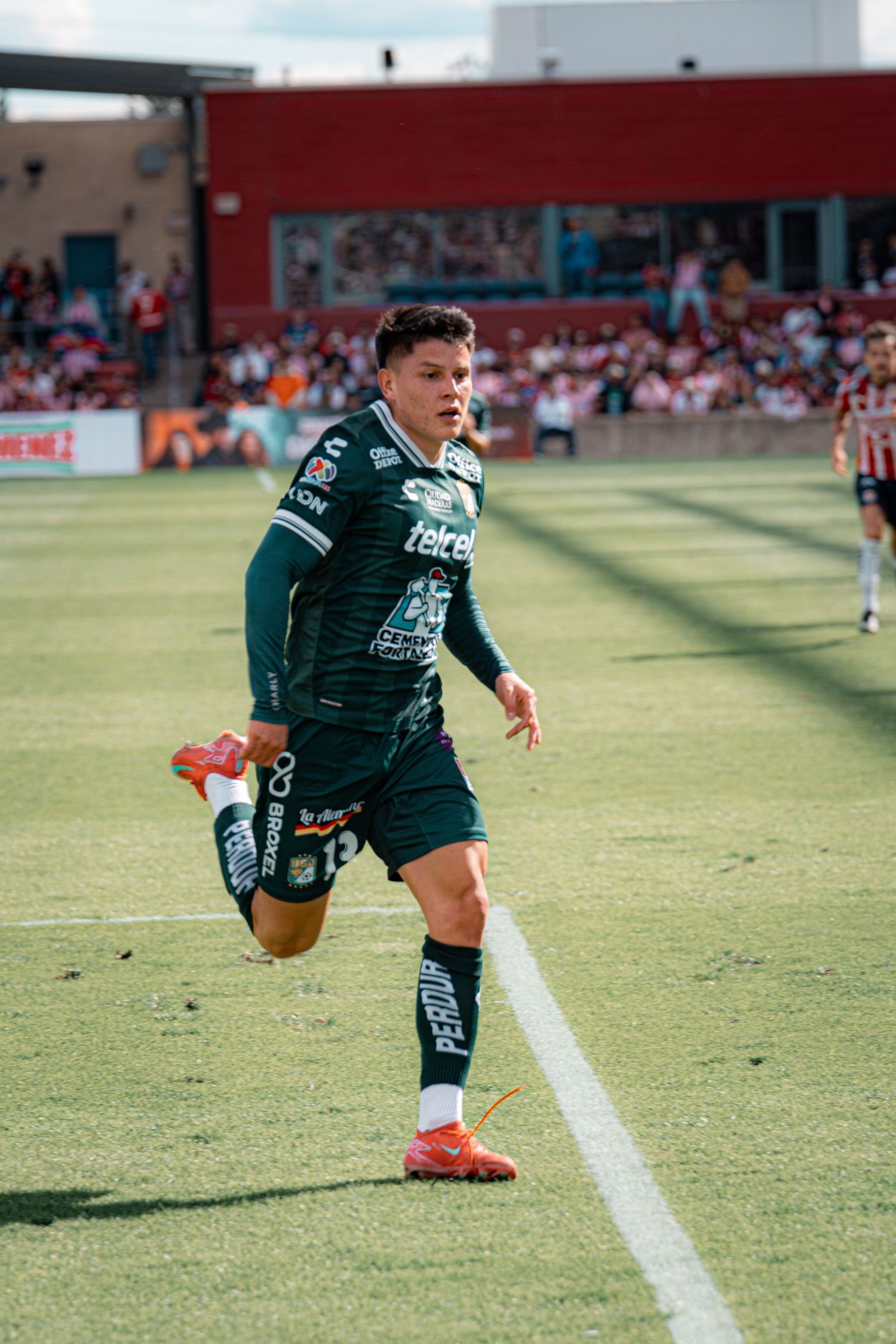 Soccer player in green jersey runs along the sideline during match play.