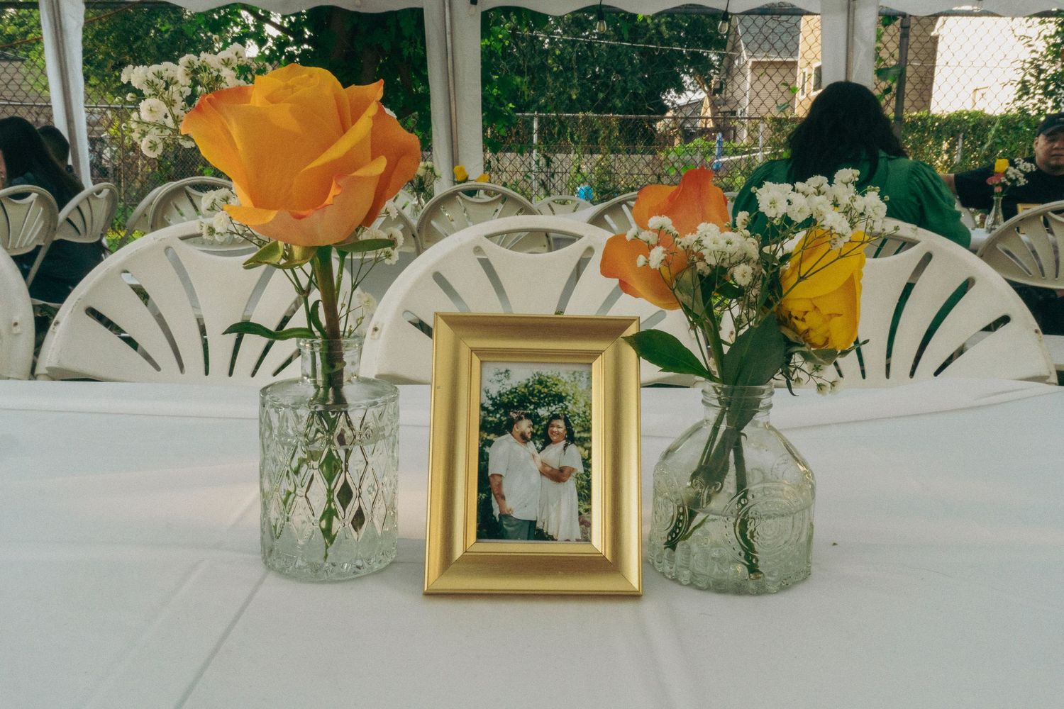 Yellow roses and baby's breath flowers arranged in glass vases with gold frames on a white tablecloth.