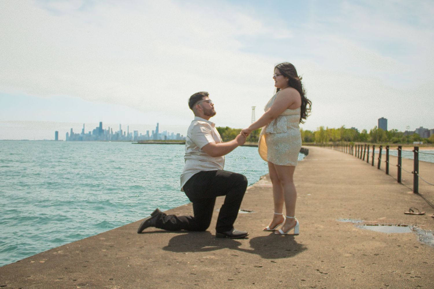 A couple sits on a concrete pier overlooking a city skyline across the water.