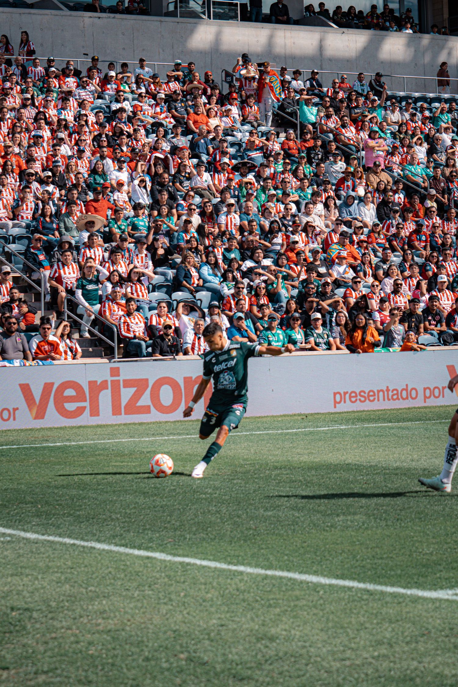 Soccer player dribbles ball during match with packed stadium crowd visible in background.
