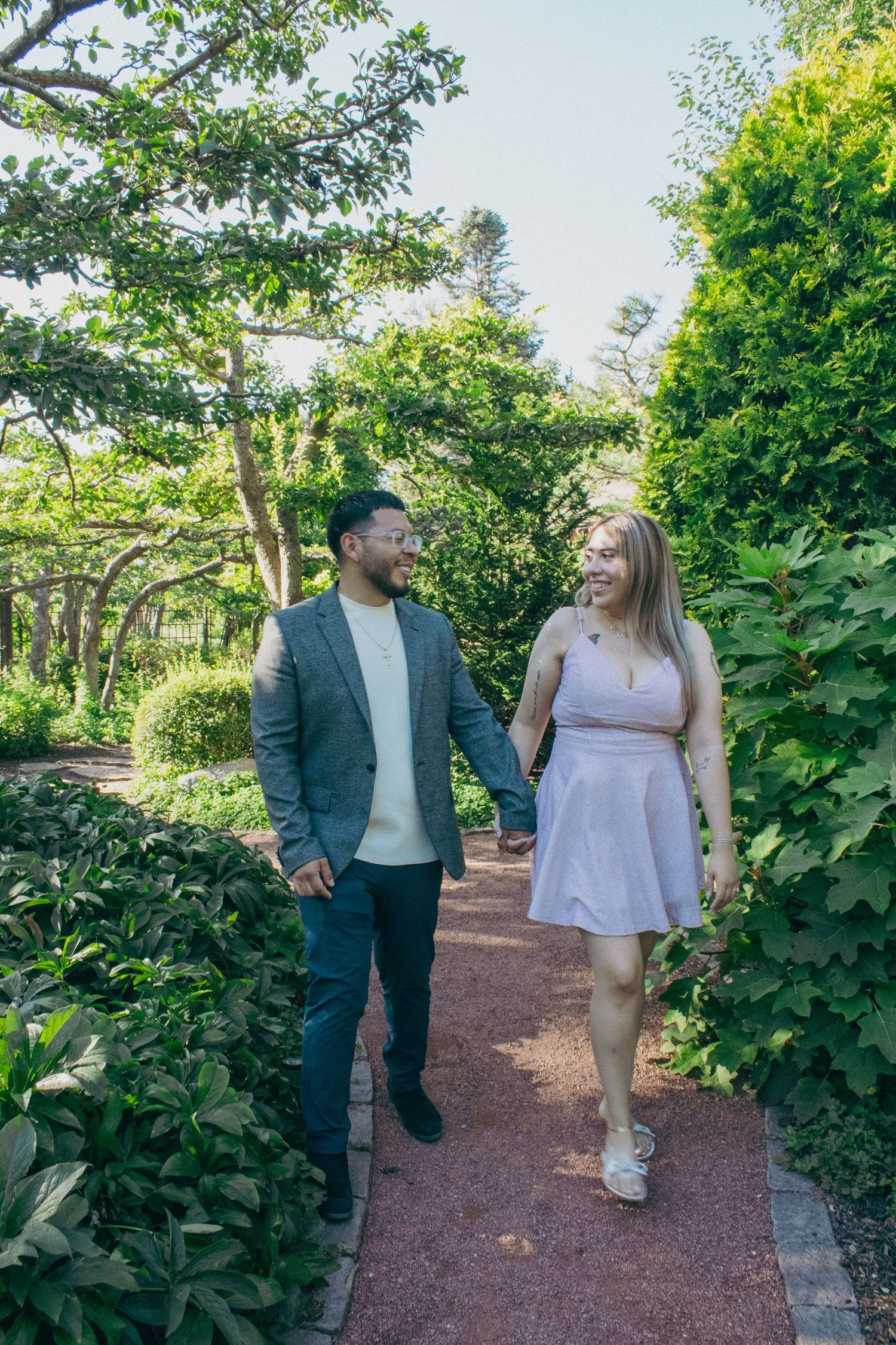Couple walking together on a garden path surrounded by lush greenery.