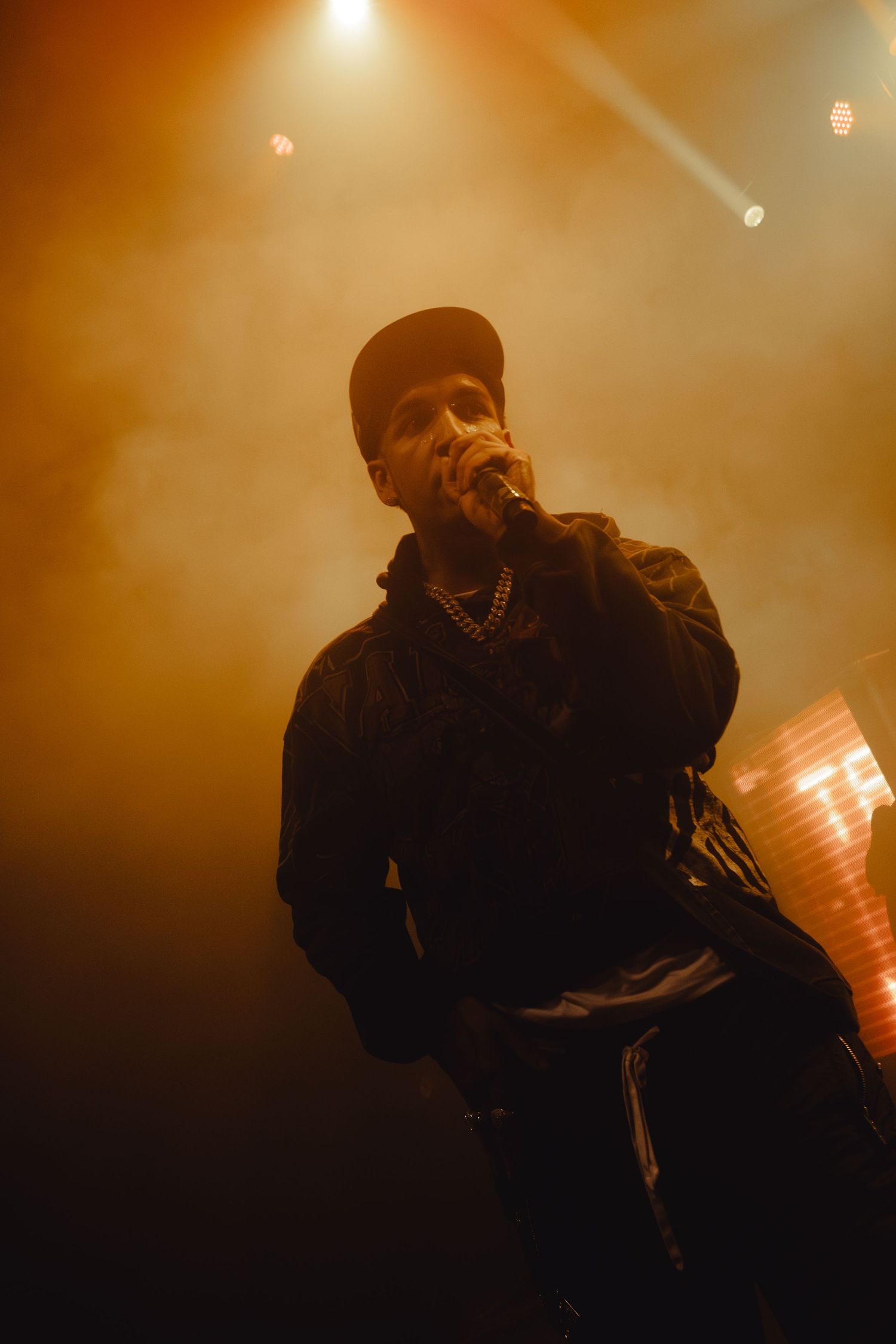 Concert performer in dark attire silhouetted against warm orange stage lighting.