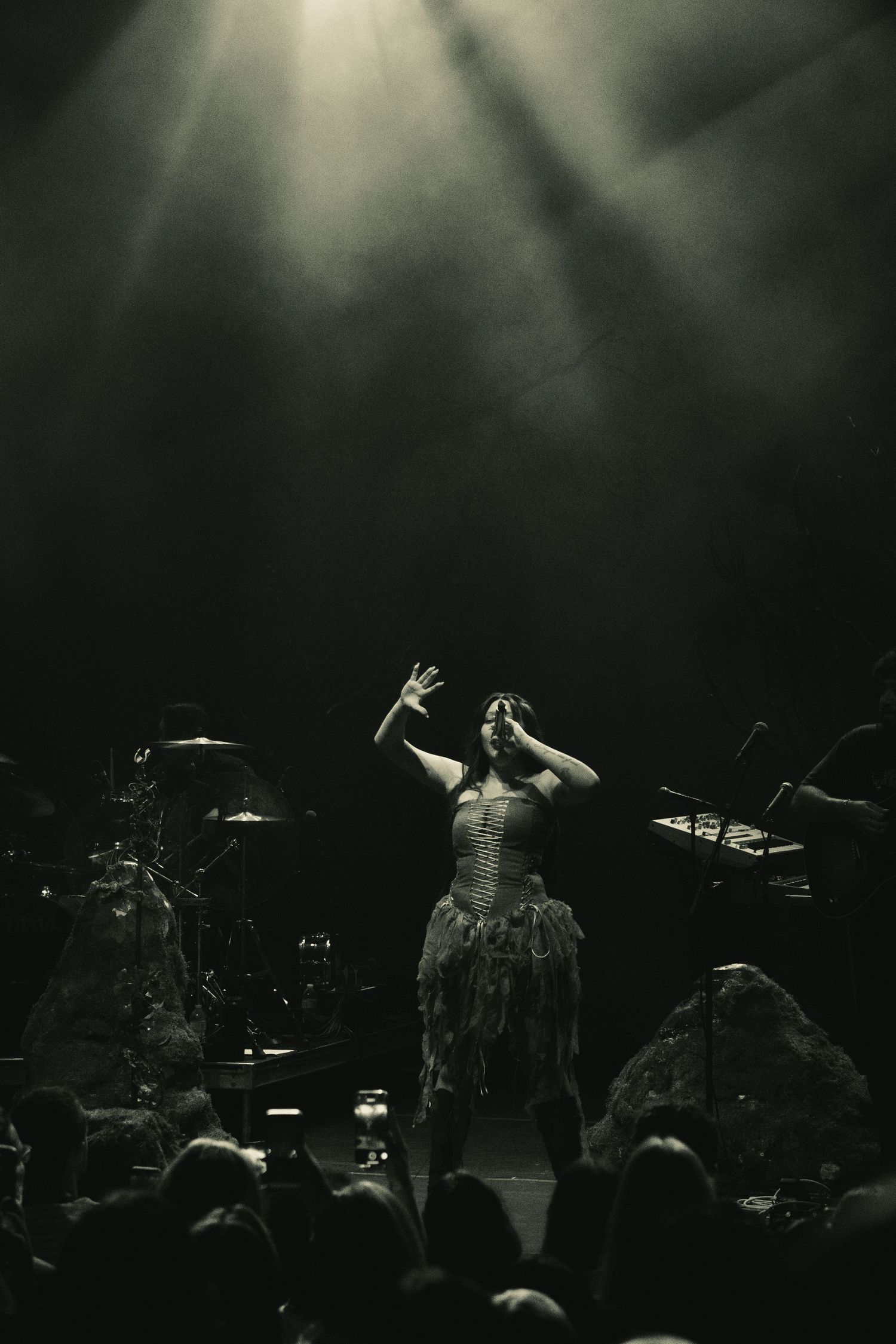 Silhouetted performers on a dark stage with dramatic beams of light shining down through atmospheric haze.