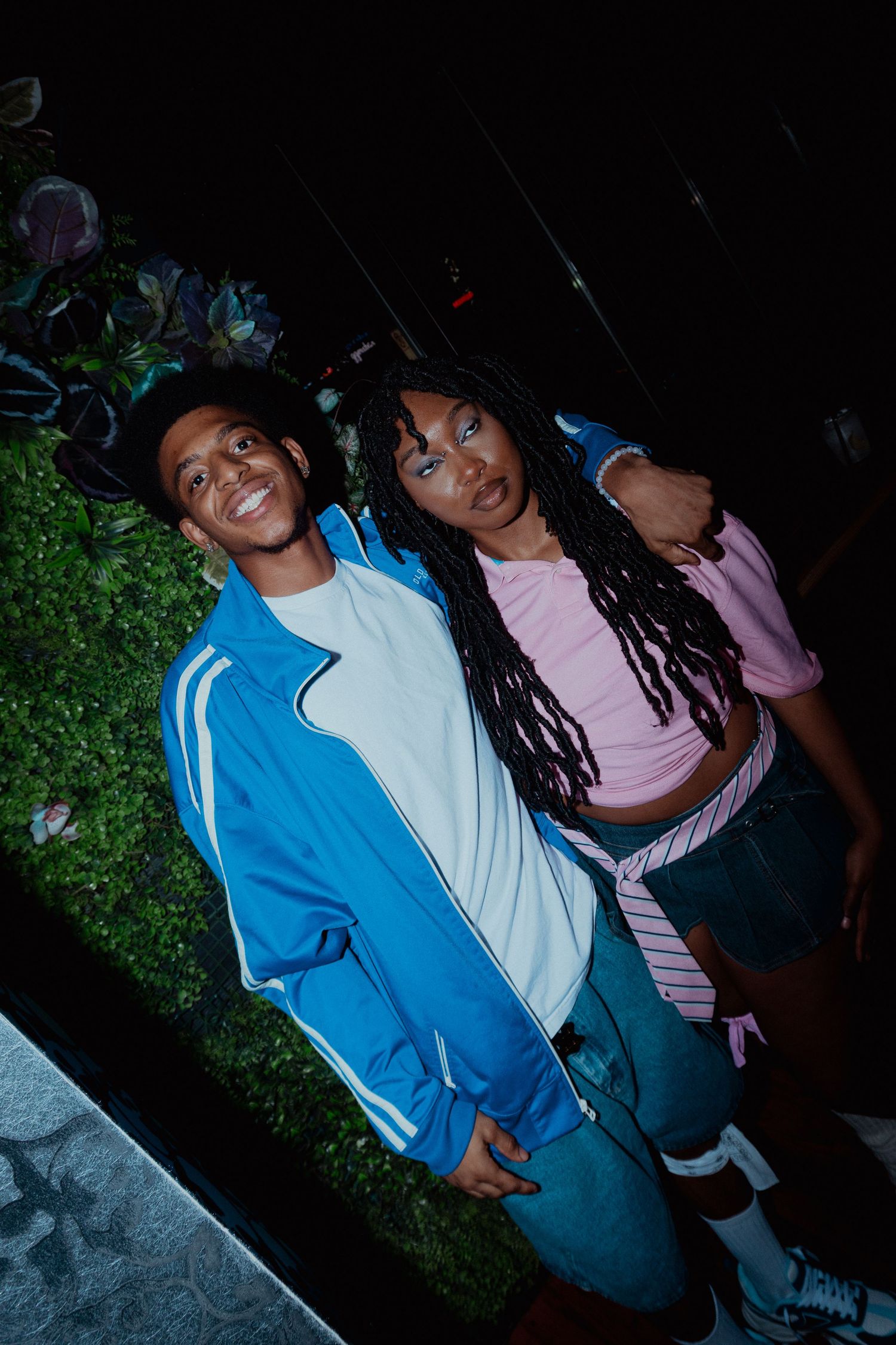 Two friends pose together at night wearing casual athletic wear in blue and pink.