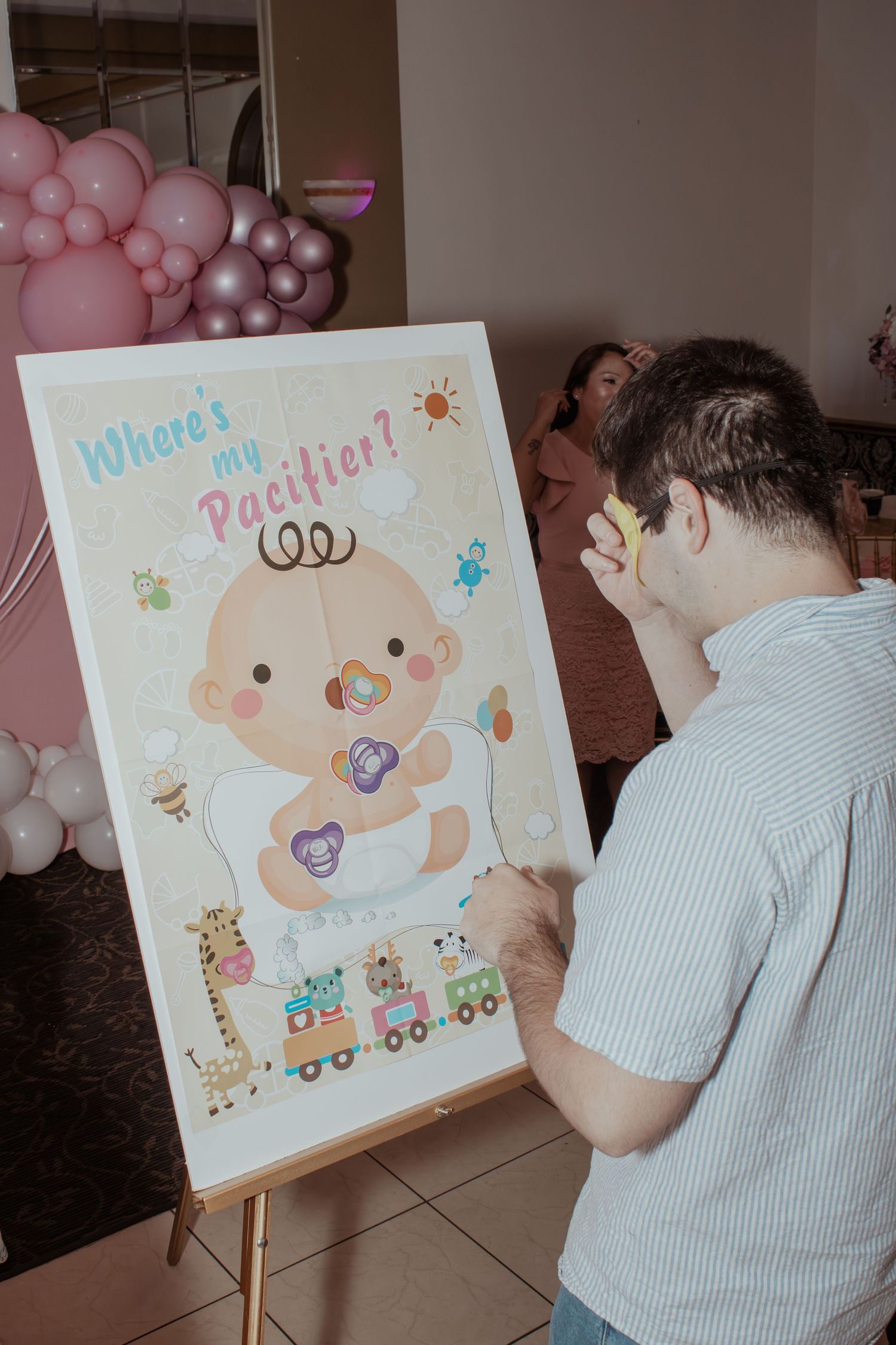 Baby shower decorations featuring cartoon illustrations on easels with pink and purple balloons.