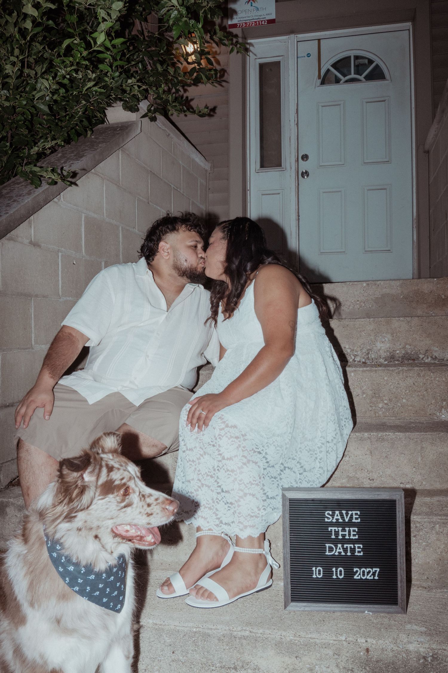 Engagement photo with couple and dog on front porch steps with save the date sign.